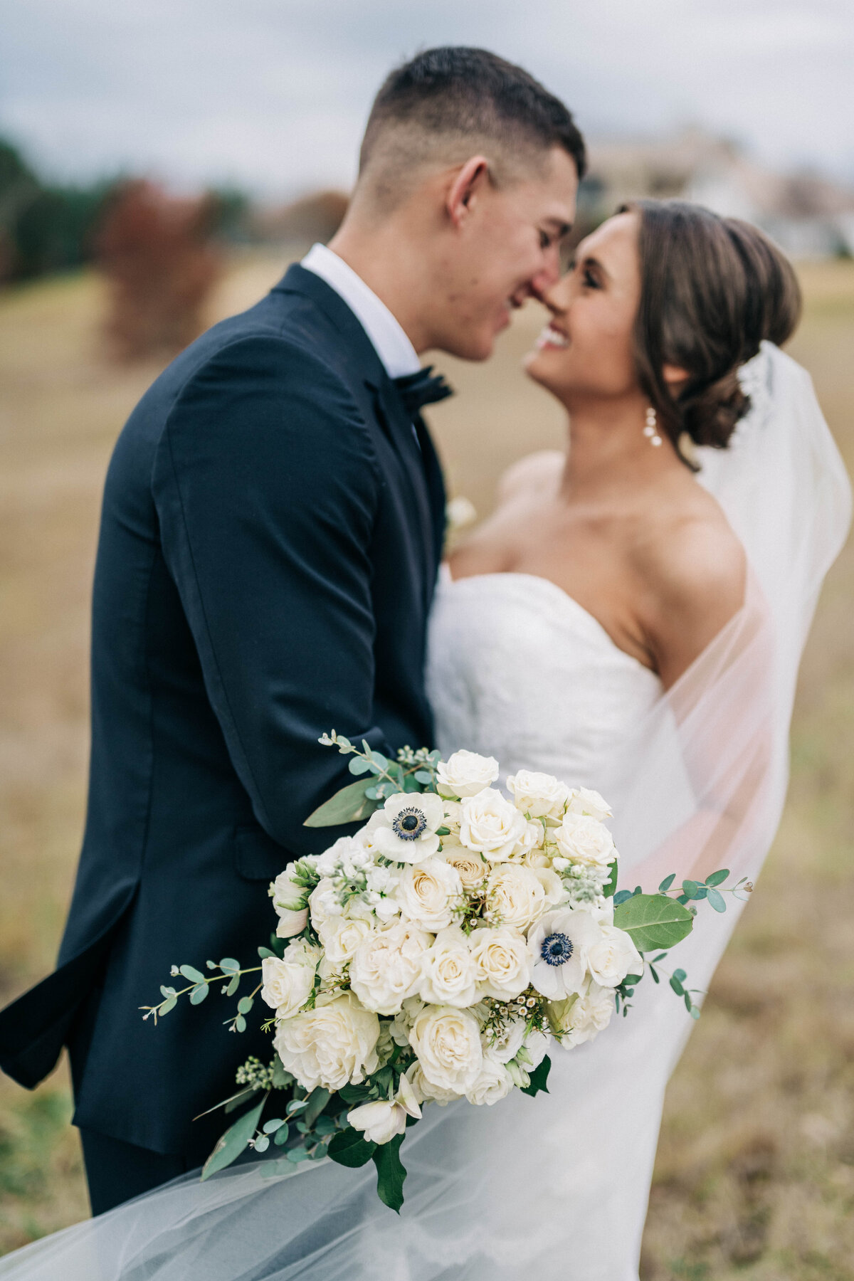Bride and groom holding each other touching noses with bouquet