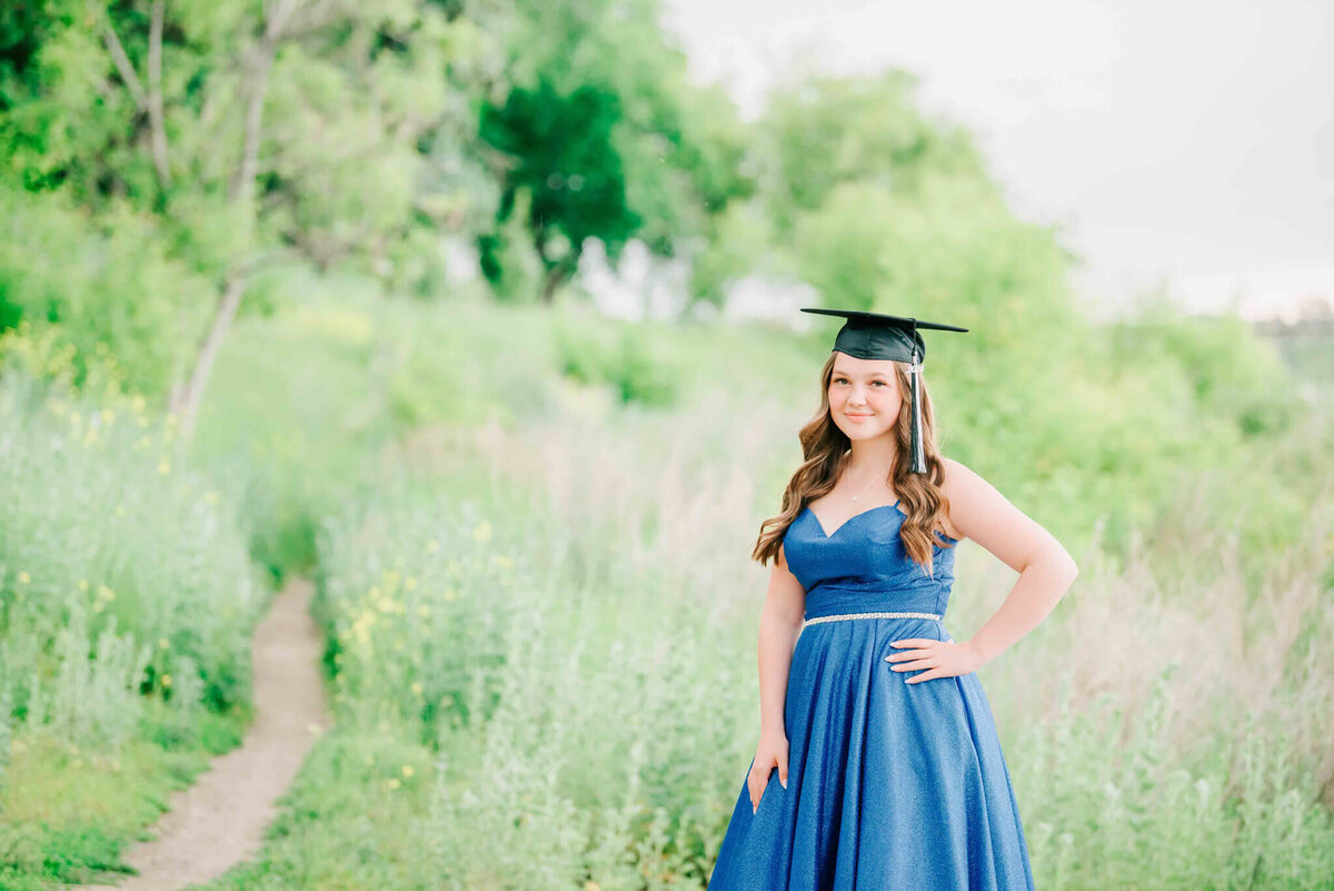 Standing in tall grass wearing a grad cap and her blue dress. 