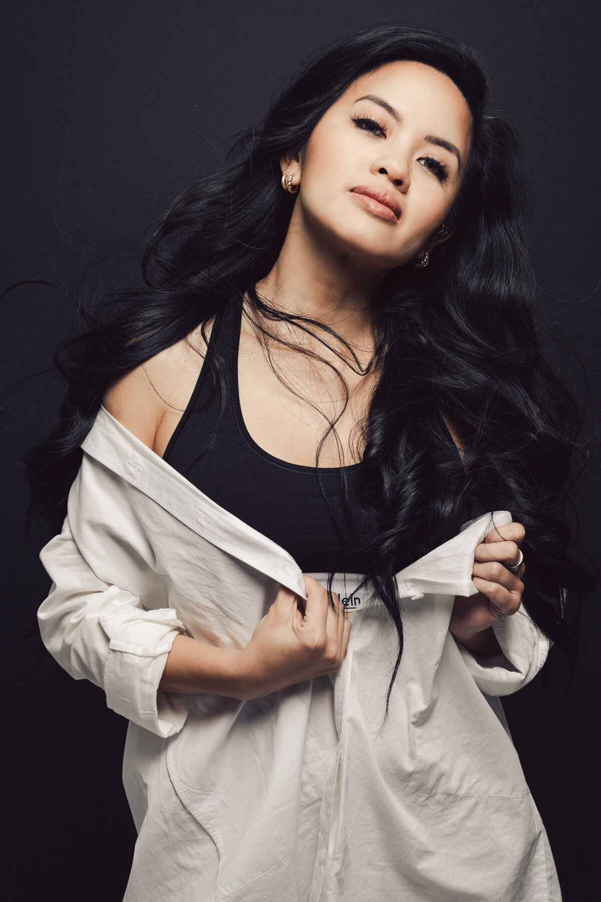 Young Asian woman in a white top unzipping it. She is in front of a black background.