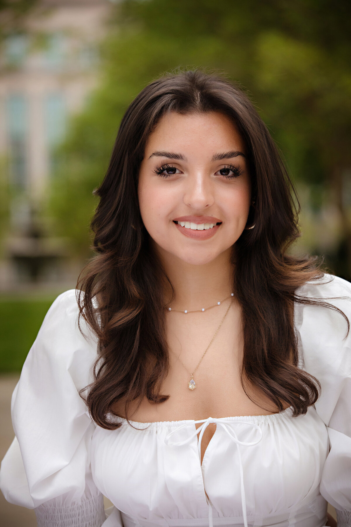 Editorial spring portrait of high school senior in white top with soft expression and urban garden elements in the background.