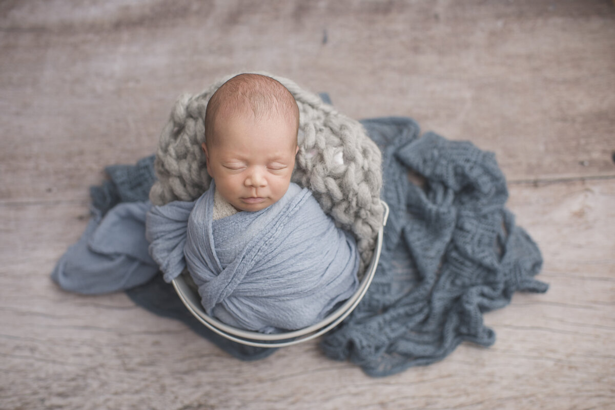 a little boy with navy blue blankets and light grey wood behind him