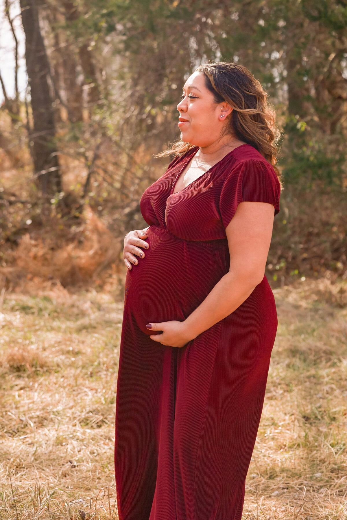 pregnant woman holding belly and wearing red dress in field with dead grass