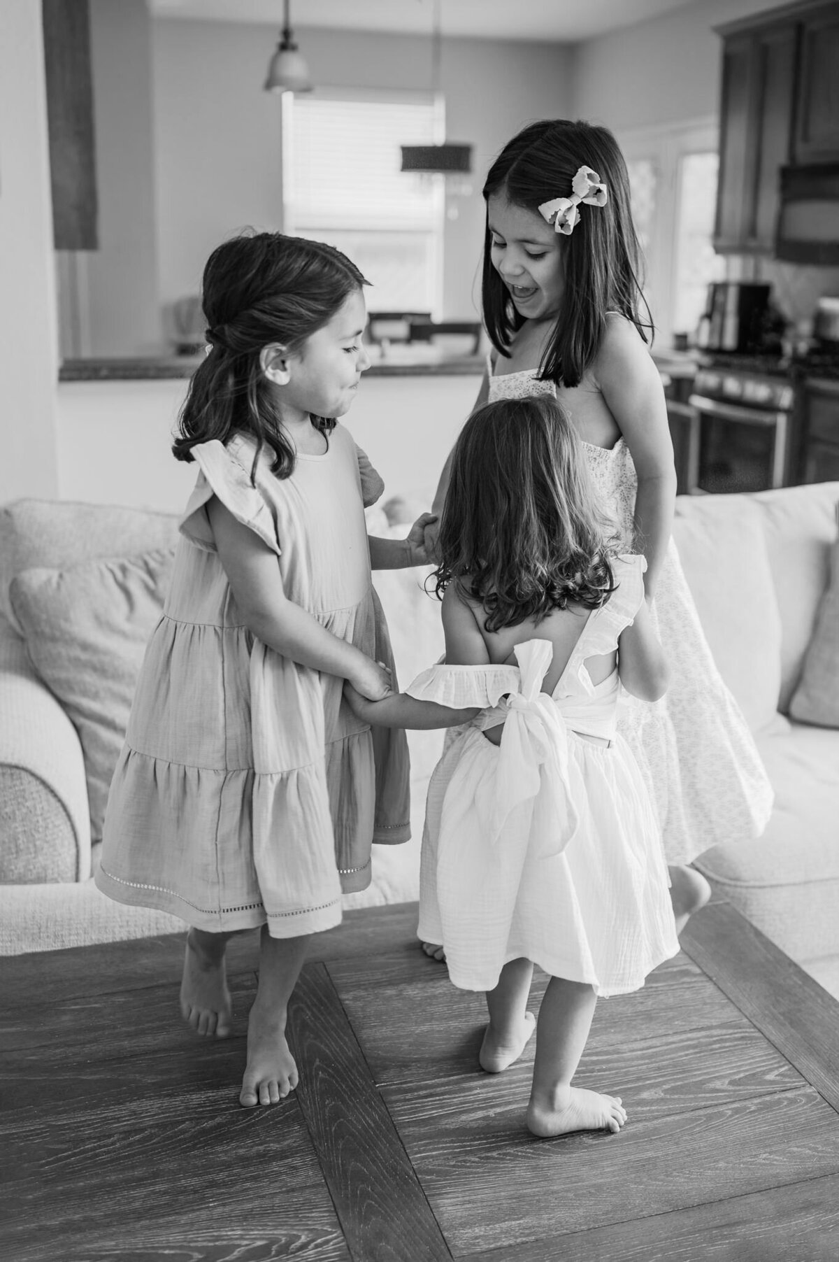 Black and white image of three young girls playing ring-around-the-rosie on their coffee table. San Antonio family photography by Cassey Golden.