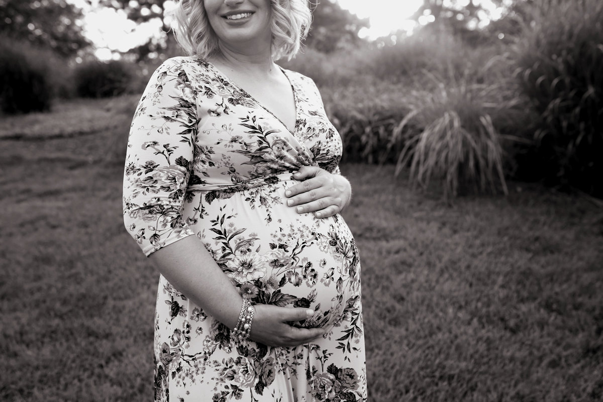 pregnant mother with hands on belly in floral dress outdoors in park