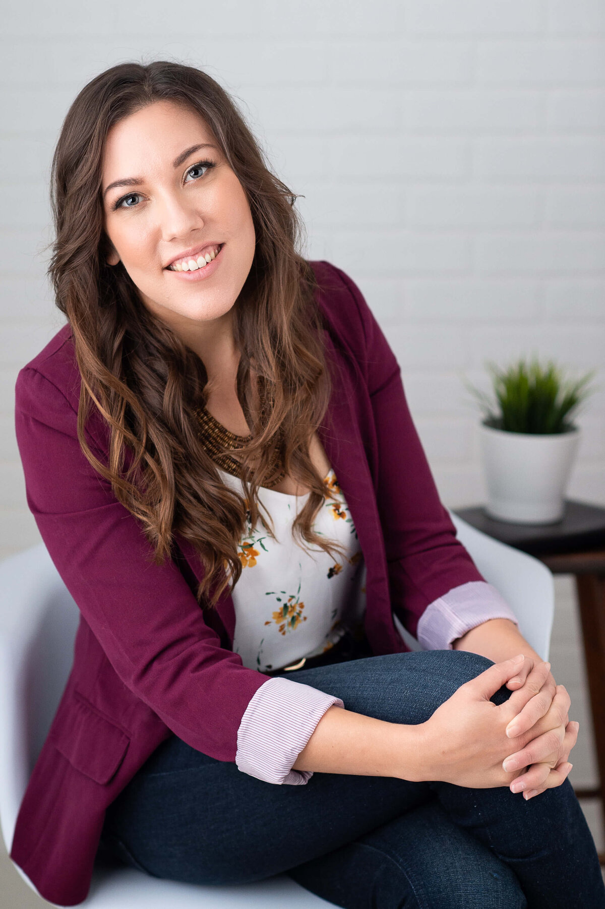 a woman in a burgundy blazer sitting with her legs crossed in a white chair.  Captured in studio by Ottawa Branding Photographer JEMMAN Photography COMMERCIAL