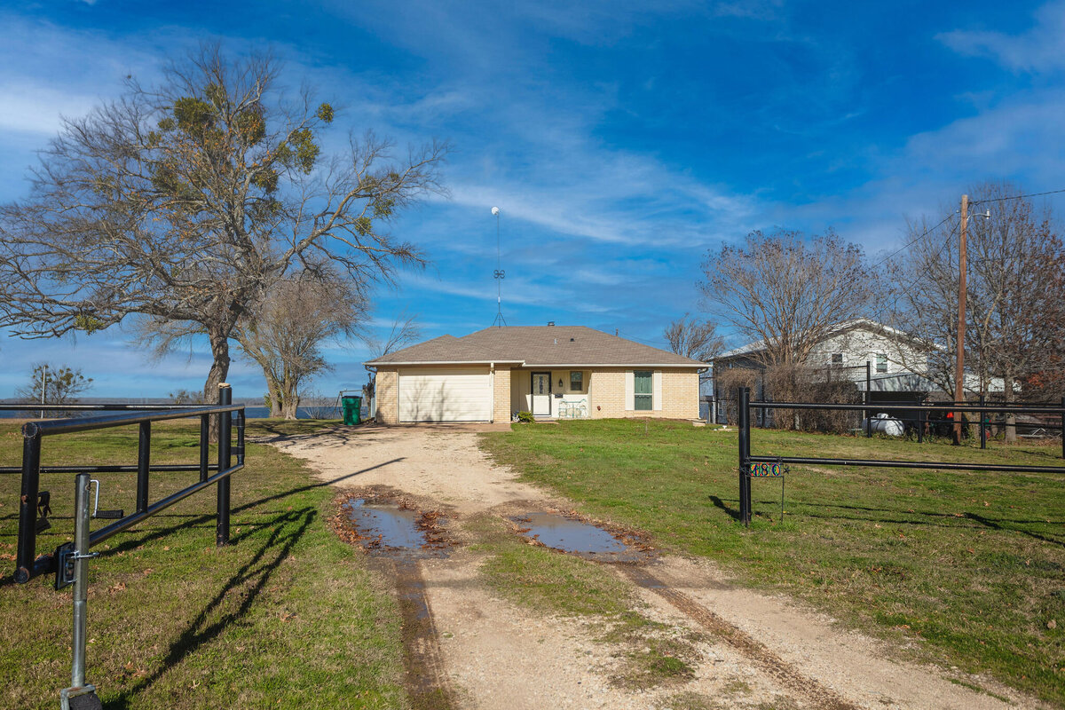 Front view of the home and gated driveway at this 2-bedroom, 2-bathroom lakeside vacation rental home for 6 guests on Tradinghouse Lake with privacy access to a fishing dock and boat launch pad, ping pong table, gazebo, free wifi and free parking in Waco, TX.