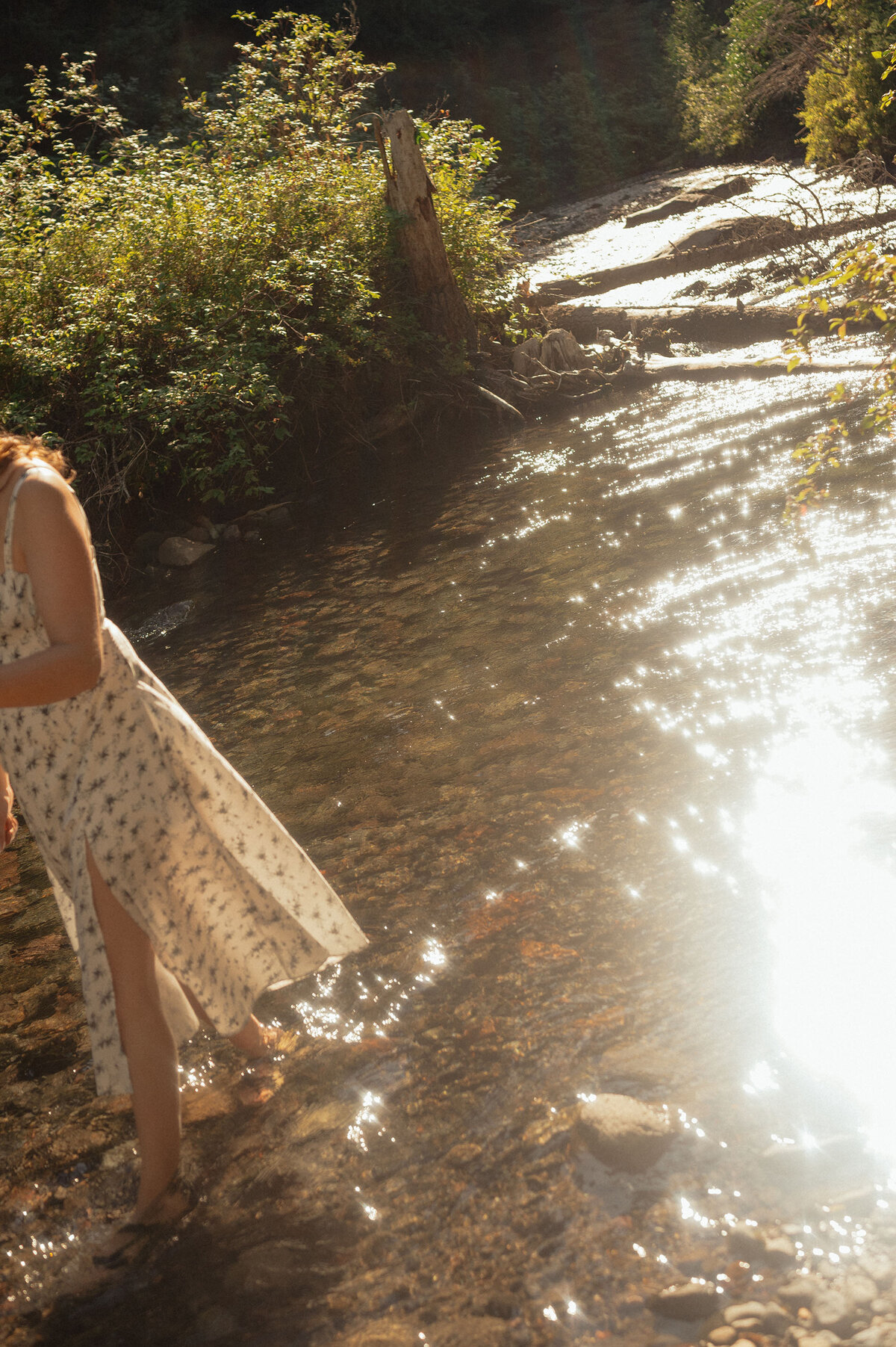 woman in white dress walks in the river as the sun casts a warm glow around her in Bend, Oregon