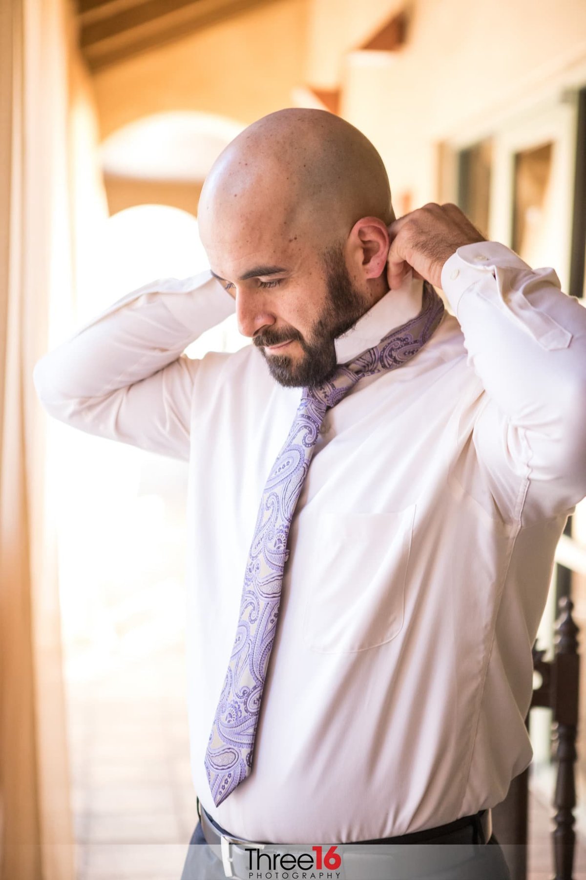 Groom puts on his tie as he dresses for his wedding