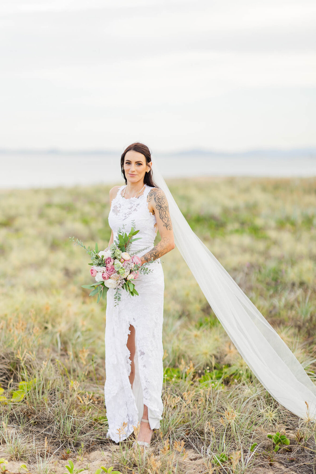 bride stands among during for a portrait looking while her veil is in the wind.