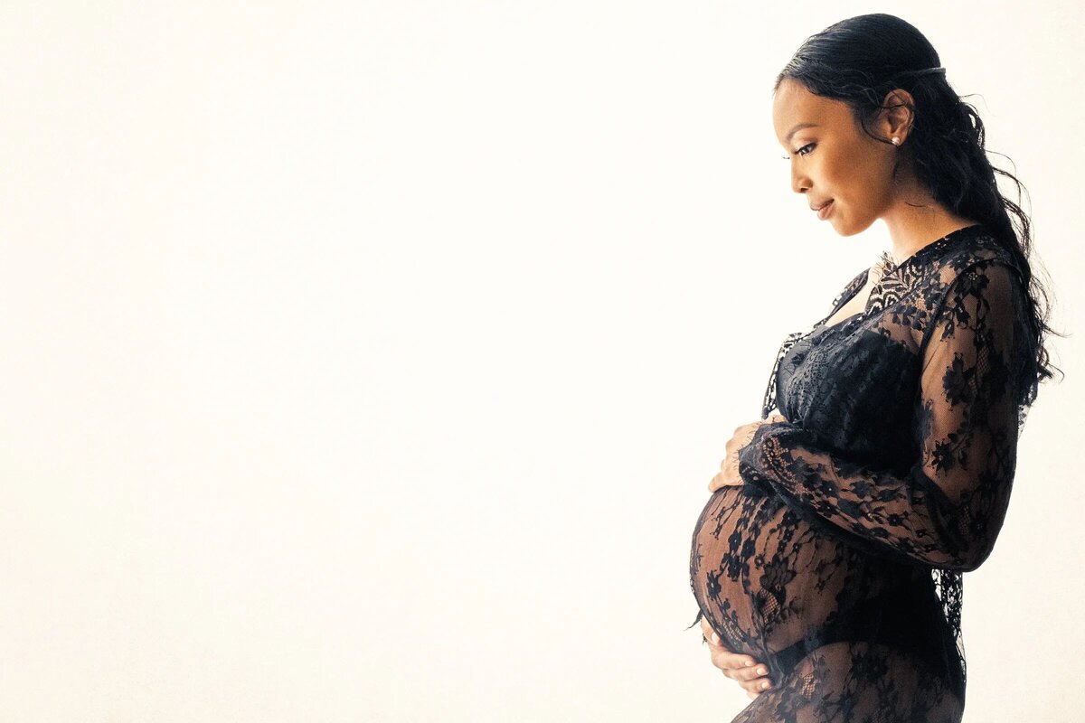 A woman in a lace dress with her hands around her pregnant stomach.