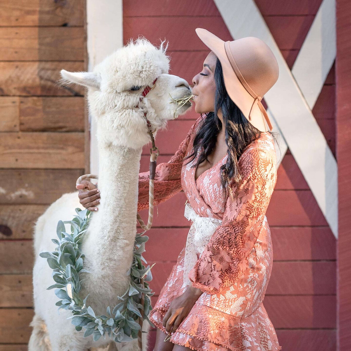 girls wearing a hat kissing an alpaca on her senior photo session at Lost mountain alpaca ranch, powder spring Georgia