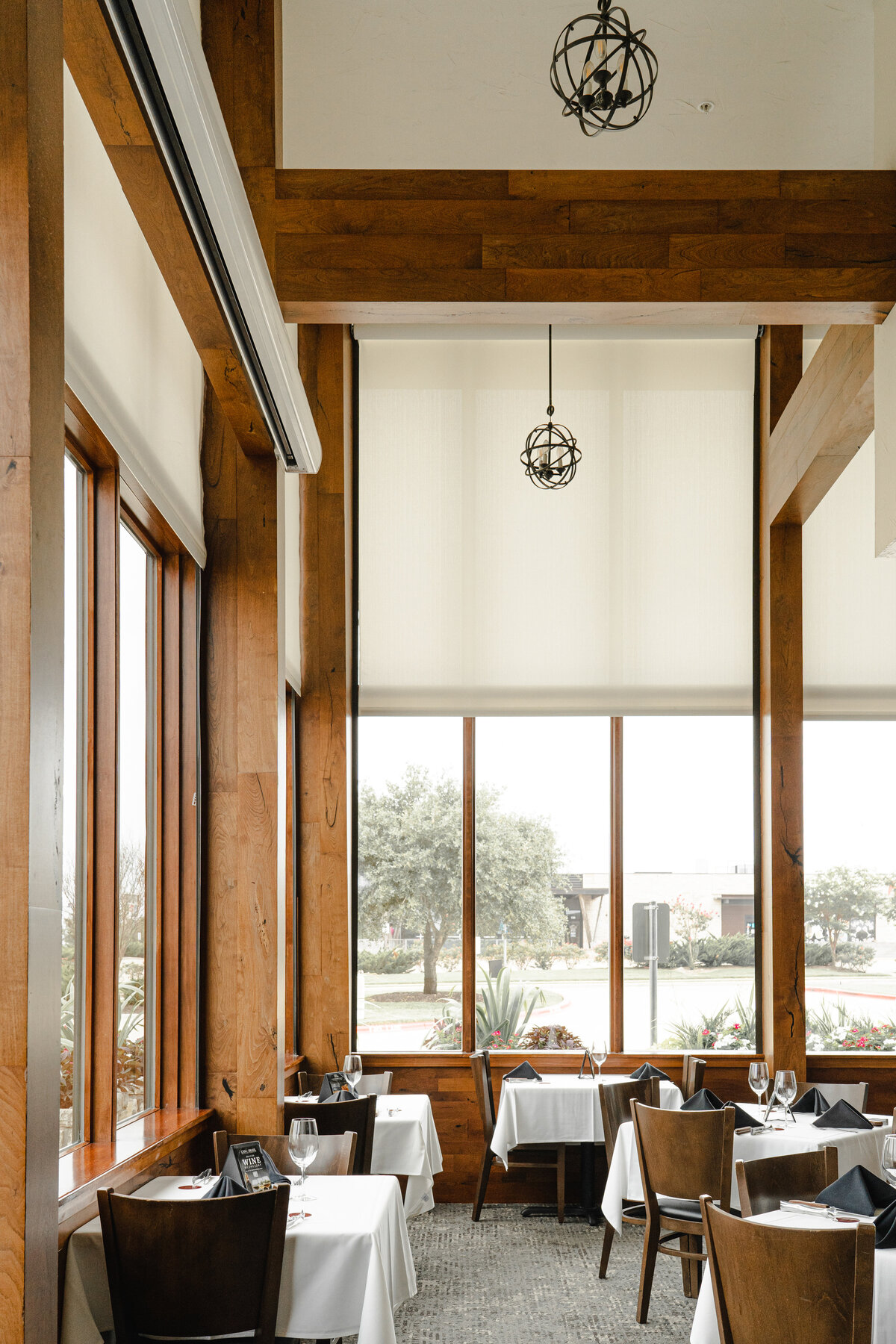 Interior of restaurant with wood paneling, tall ceilngs, tall windows and white motorized shades