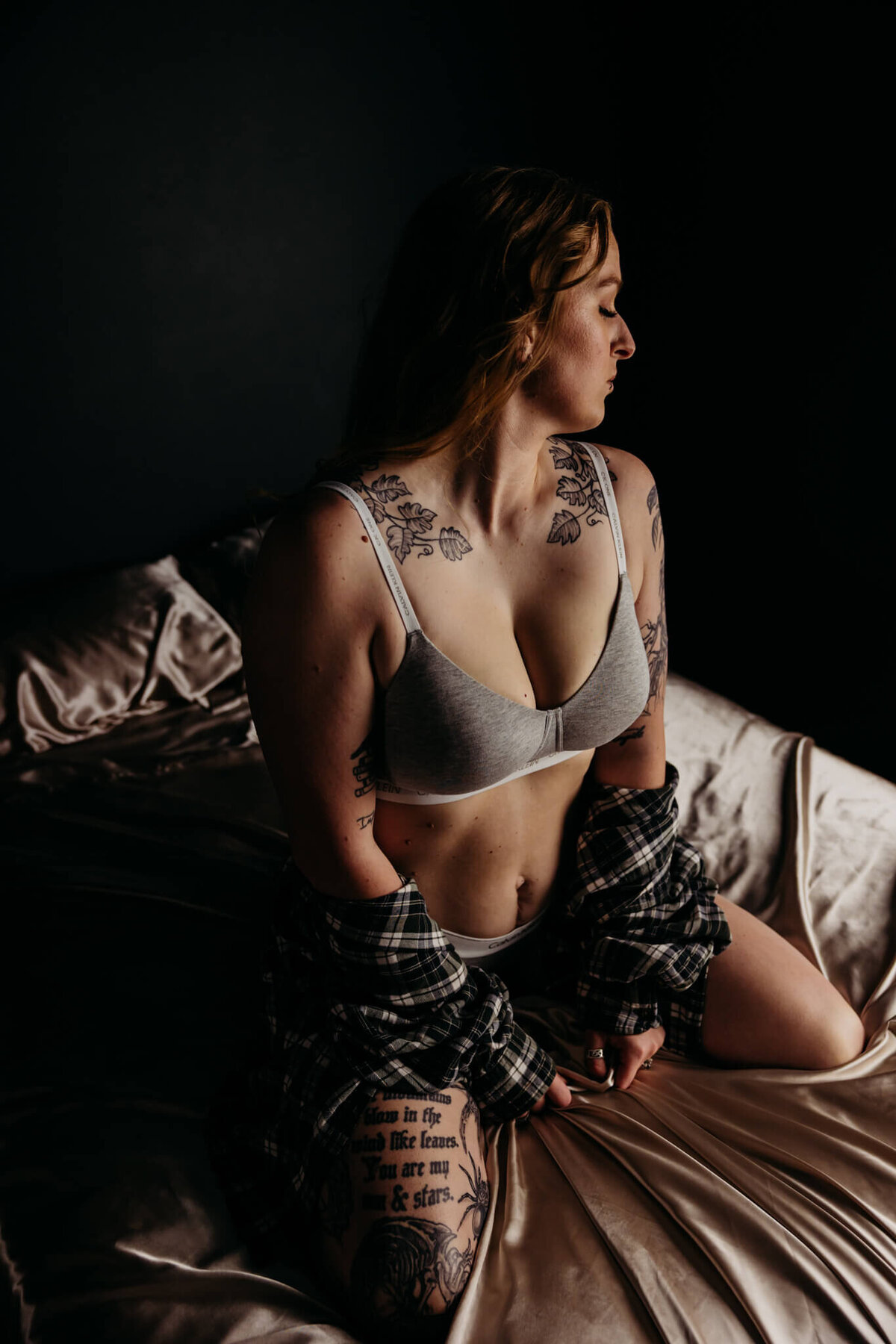 pretty female in a grey calvin klein set wrapping herself in a flannel as she kneels on a bed and looks over her shoulder in a studio near Oshkosh