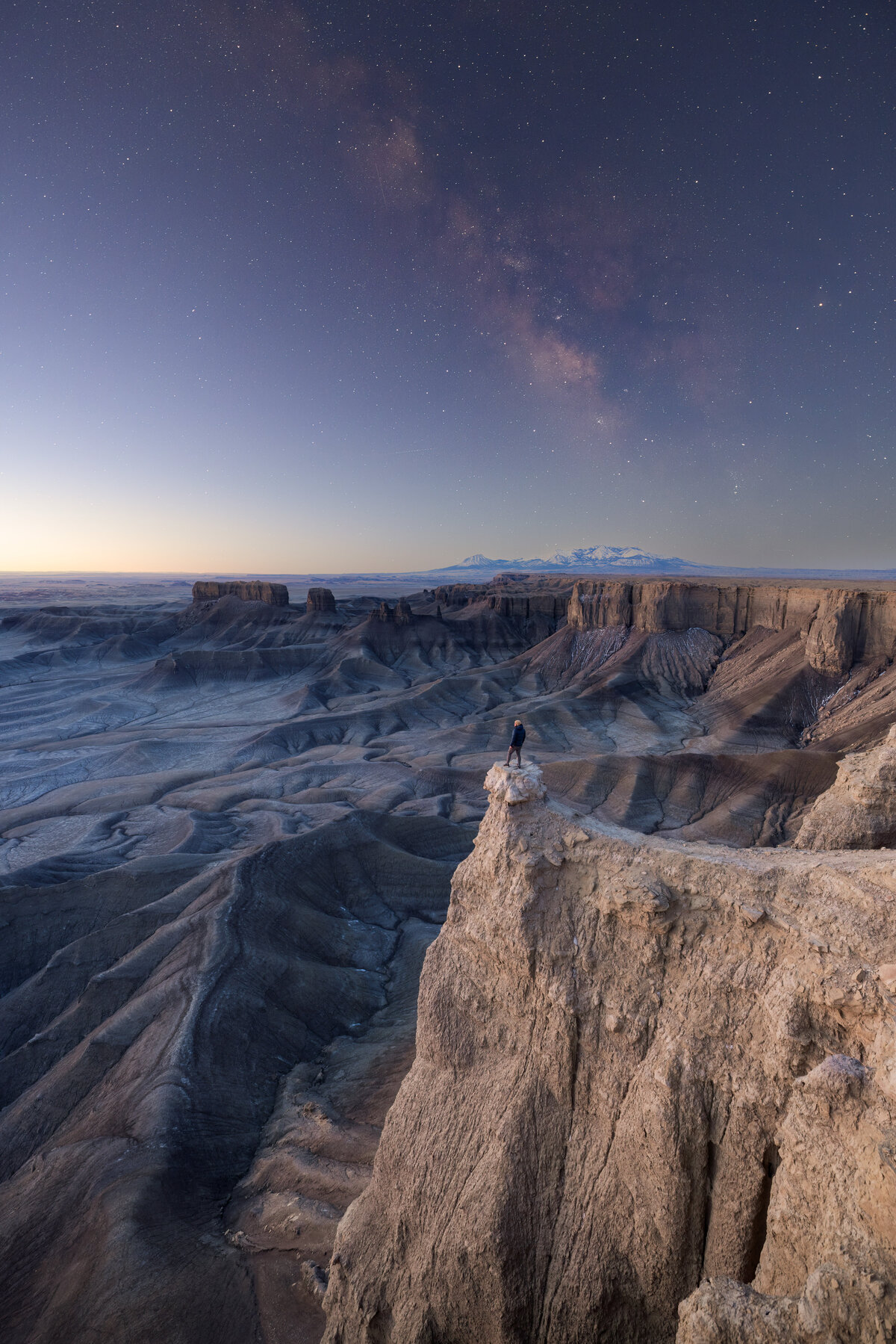 A man standing on the Moonscape overlook in Hanksville, Utah during sunrise; the last sight of the Milky Way galaxy above him