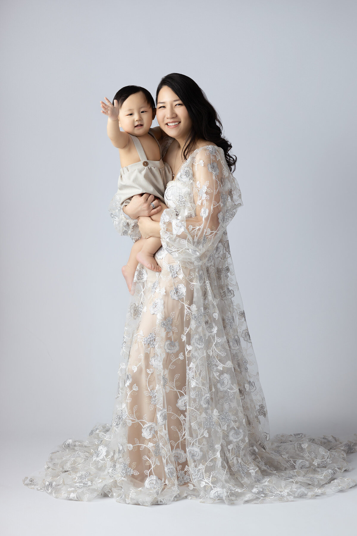 Dallas baby milestone photographer captures a mother and son, both smiling joyfully, dressed in elegant outfits with a soft background.