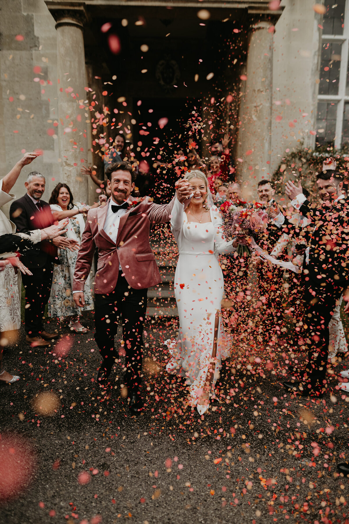 Epic pink and red confetti shot of a bride and groom being covered outside Elmore Court.
