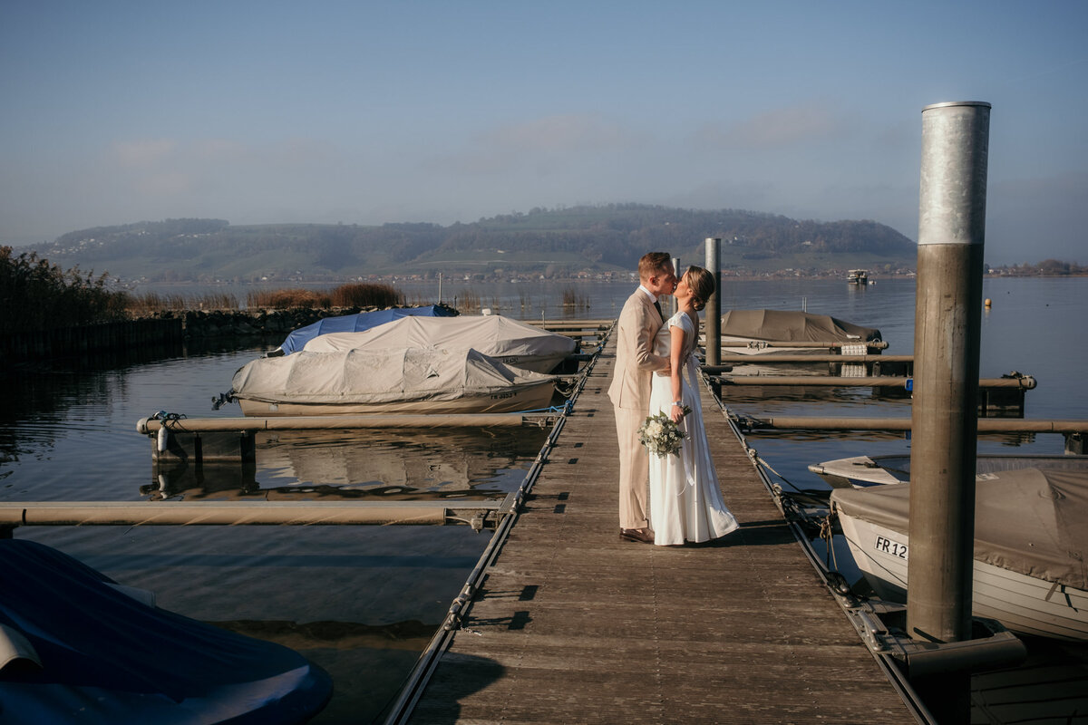 The wedding couple kisses on a footbridge in the sunshine.
