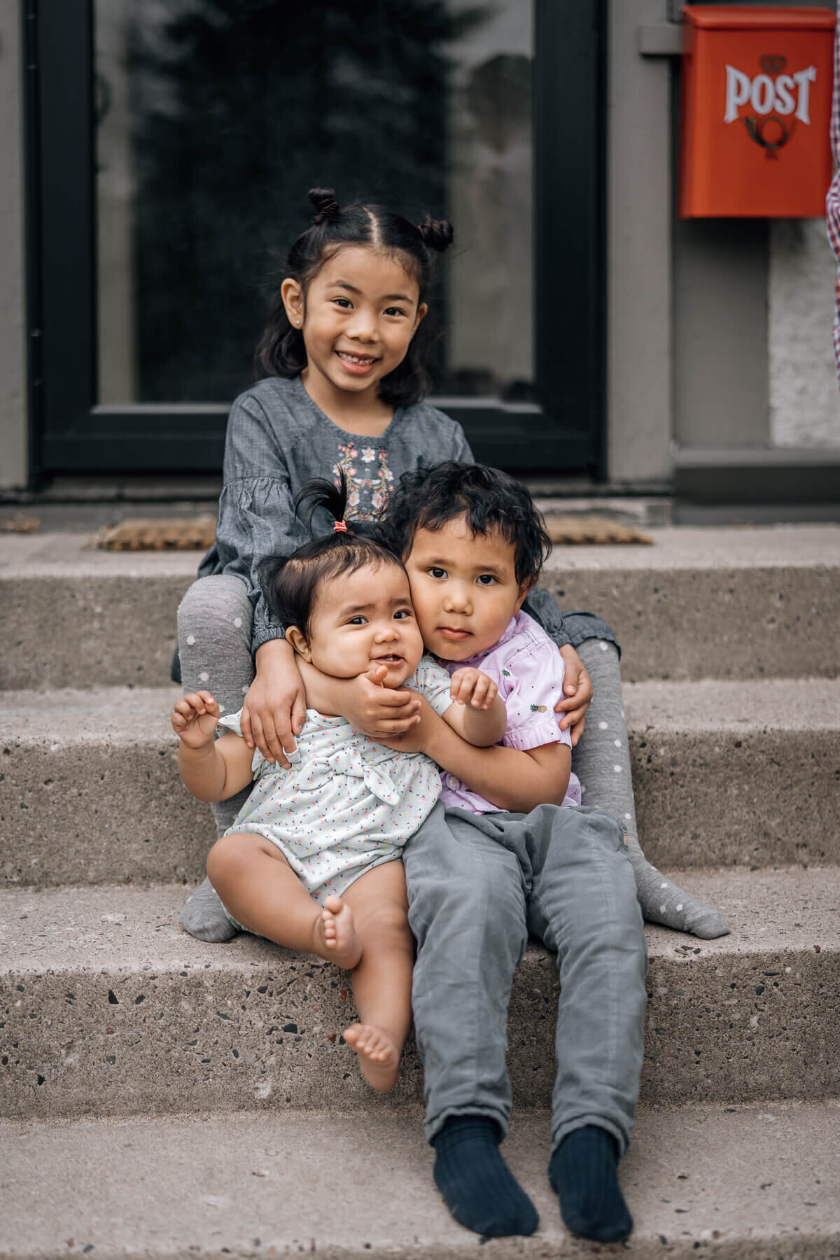 Three siblings sit together on their front porch hugging a little too tightly during an at home photography family session.