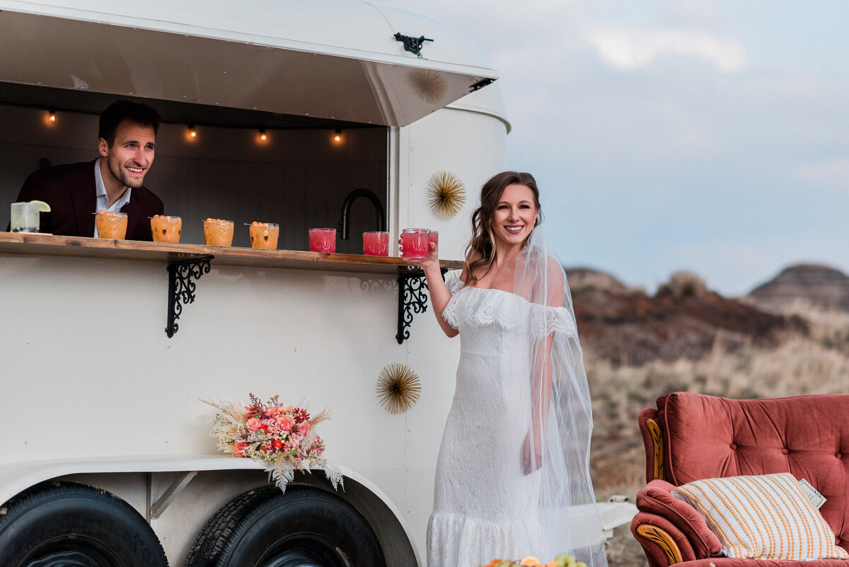 Groom makes bride a drink in a mobile bar after their elopement in Drumheller, Alberta.