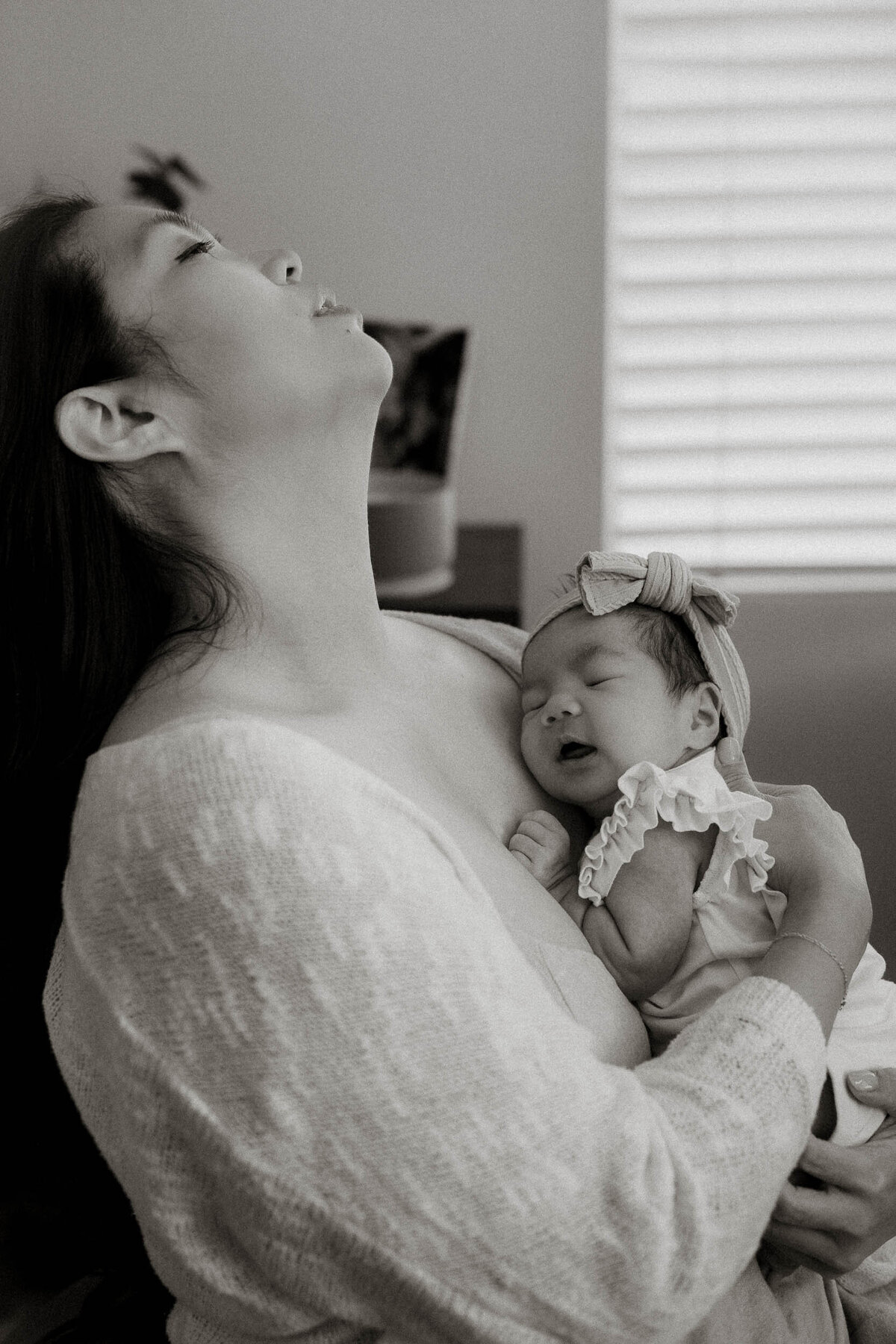 Mother cradling her newborn against her chest, leaning her head back with eyes closed in a tender, emotional moment.