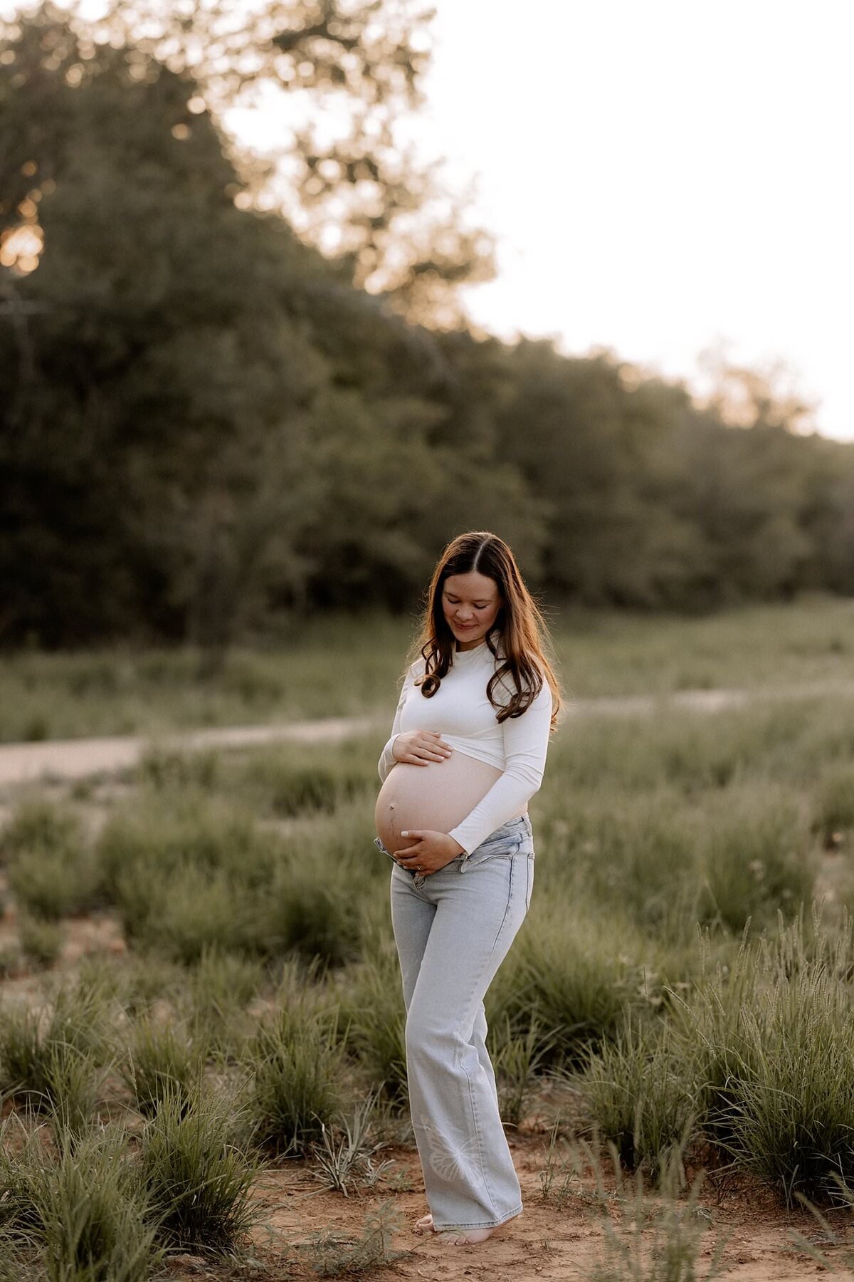 pregnant mama in a green field , she is pregnant and is wearing a tank with denim jeans