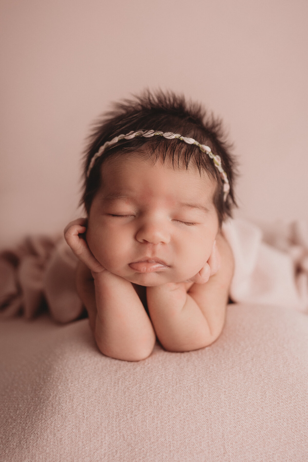 Newborn baby girl posed on pink fabric with chin on hands at Marietta newborn photography studio