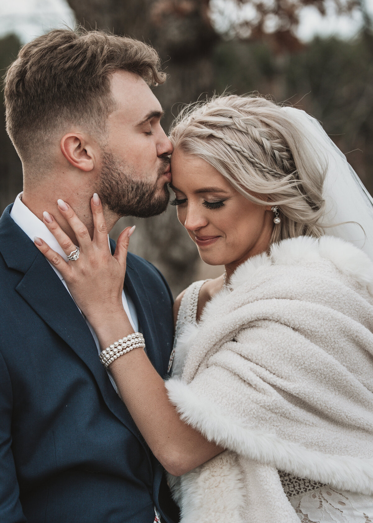 A tender moment between bride and groom as they share a gentle kiss, their love and joy palpable amidst the serene backdrop of nature and bride wearing a fur coat taken by jen  Jarmuzek photography a Minneapolis wedding photographer