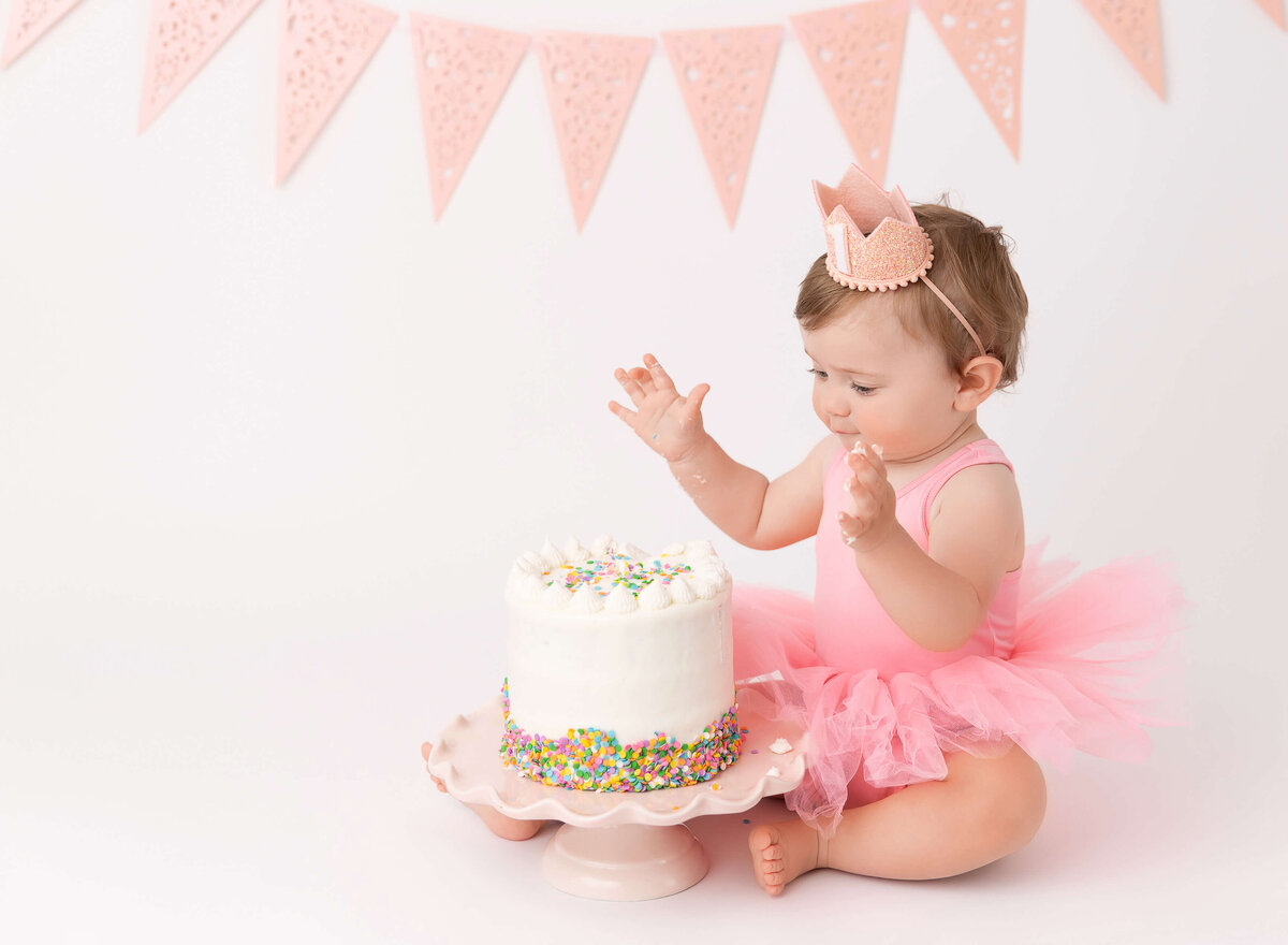 1st birthday cake smash photoshoot in New York City with pastel pink banner and playful decorations. A fun and professional session to capture special moments for your baby’s first birthday celebration
