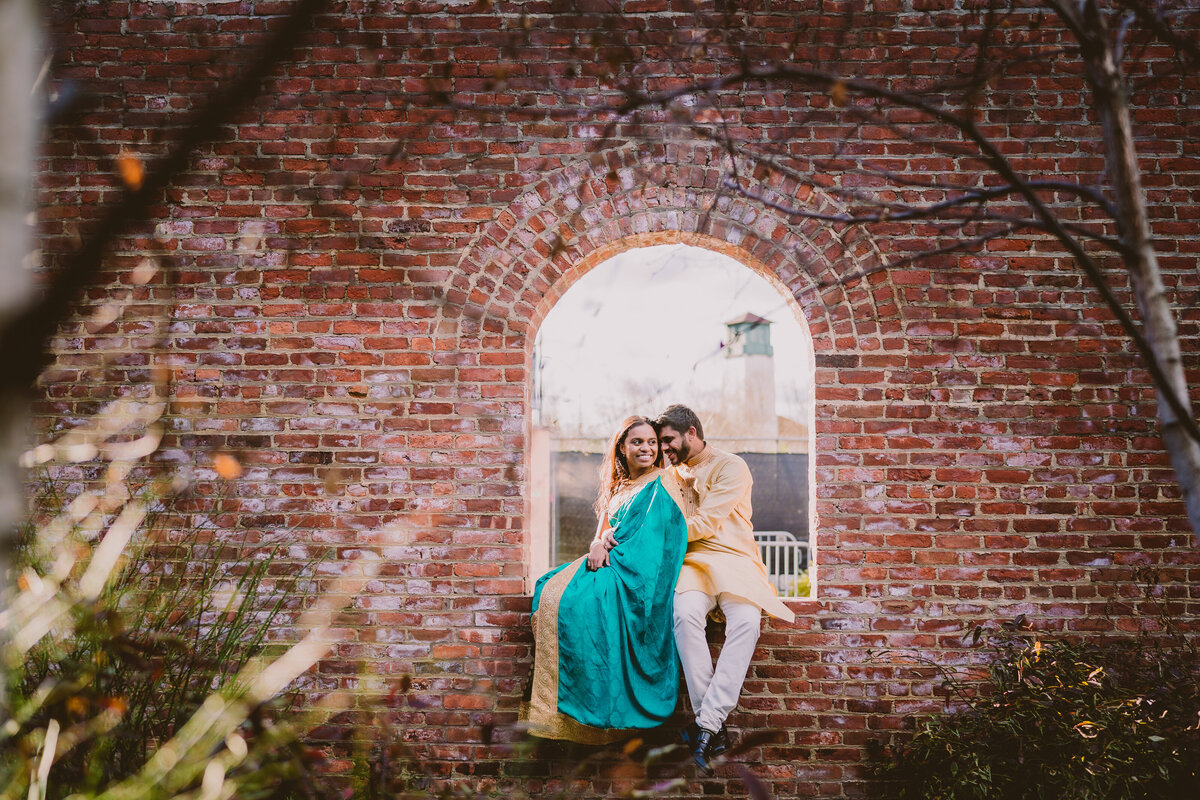A couple sitting inside the max family garden window arch brick wall in indian outfits at brooklyn bridge park