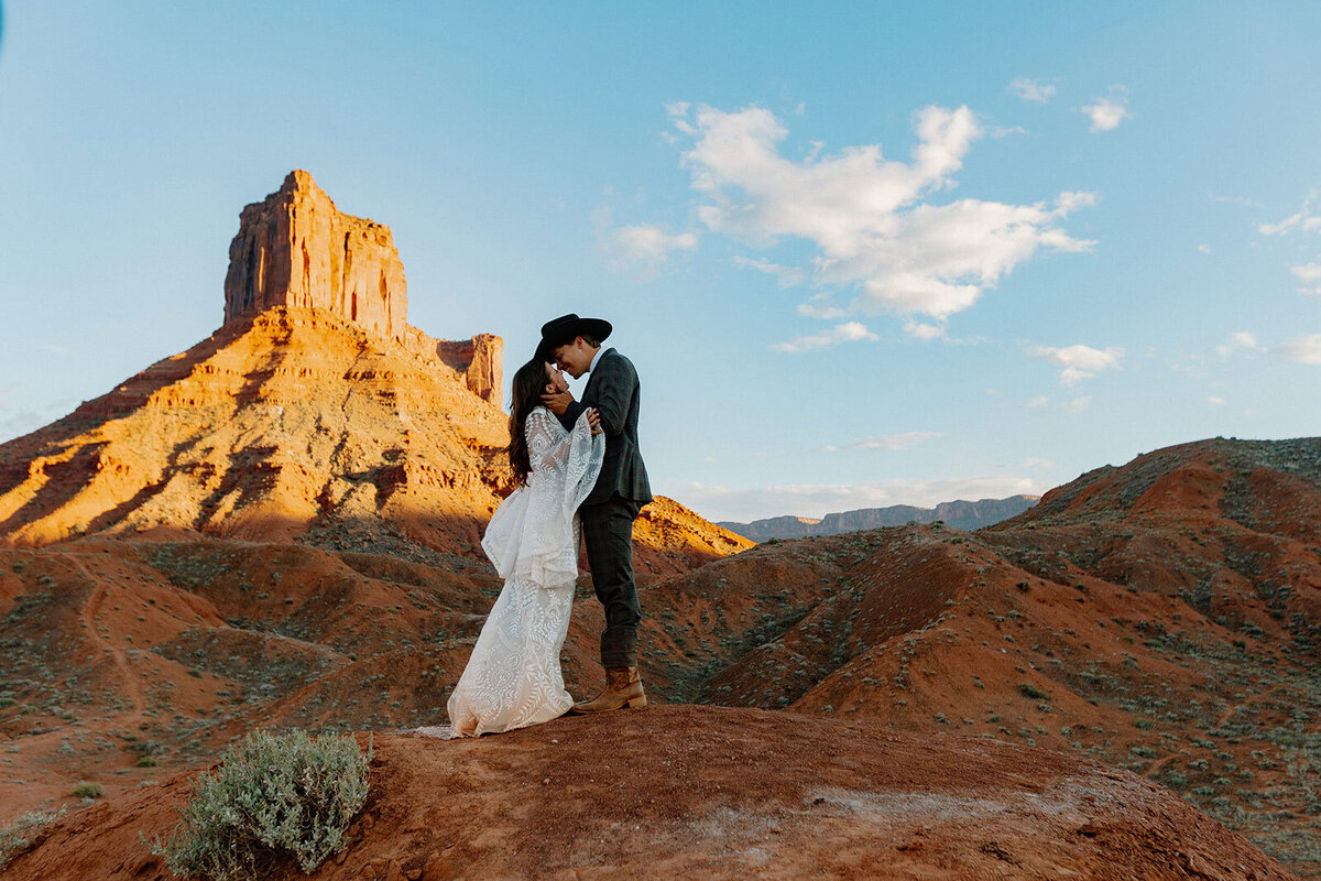 A groom in a cowboy hat, and a bride share a tender moment on their wedding day in Moab as the sun sets. 