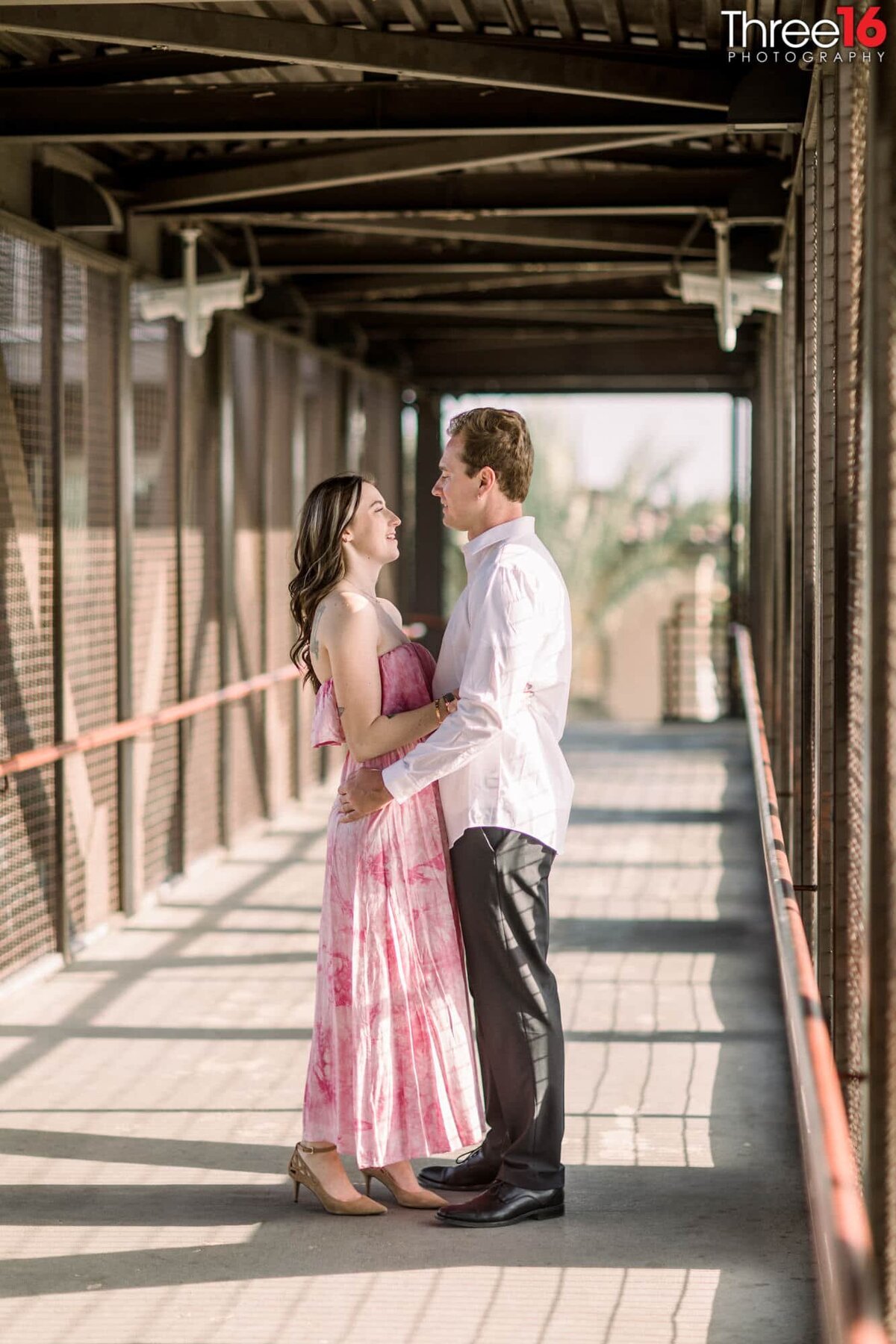 Engaged couple gaze at each other standing on a bridge over the train tracks in Fullerton