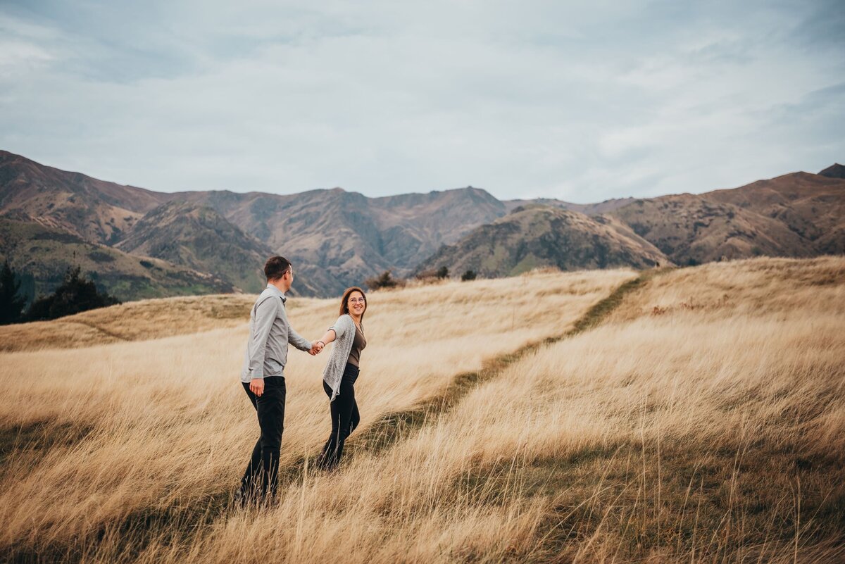 couple walking in the field during their engagement session in wanaka with Captured by Bie