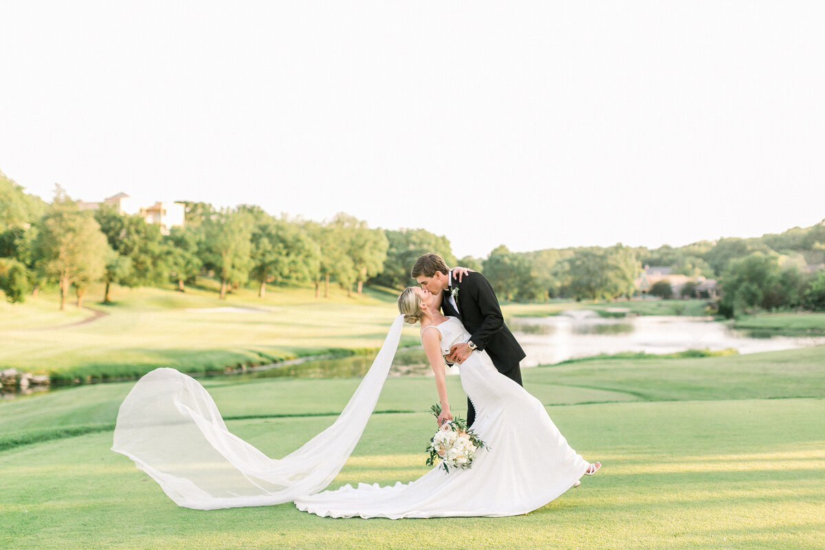 joyful-couple-at-their-greenhouse-two-rivers-wedding-in-springfield-mo-groom-whispering-into-brides-ear-bride-blowing-veil-black-and-while-image-by-branson-wedding-photographer-kathryn-faye-photography