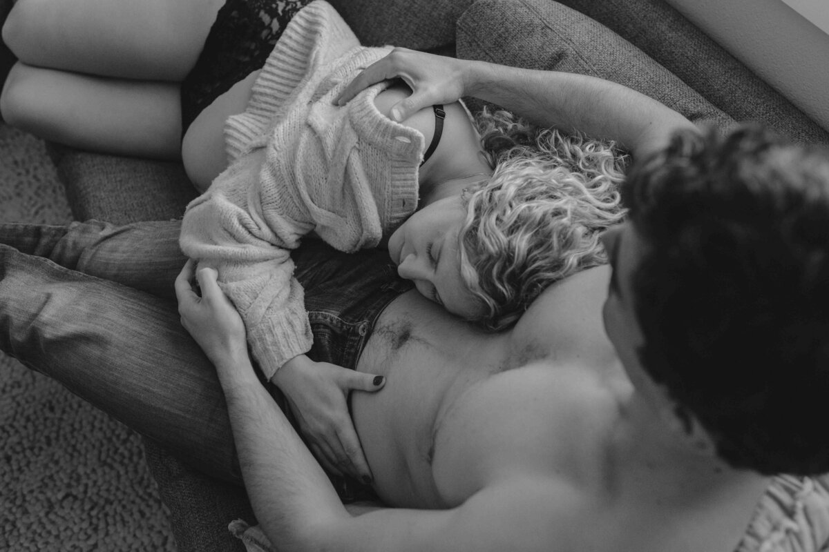 Black and white image of soon to be parents cuddling on the couch during a home maternity photoshoot in Portland, Oregon.