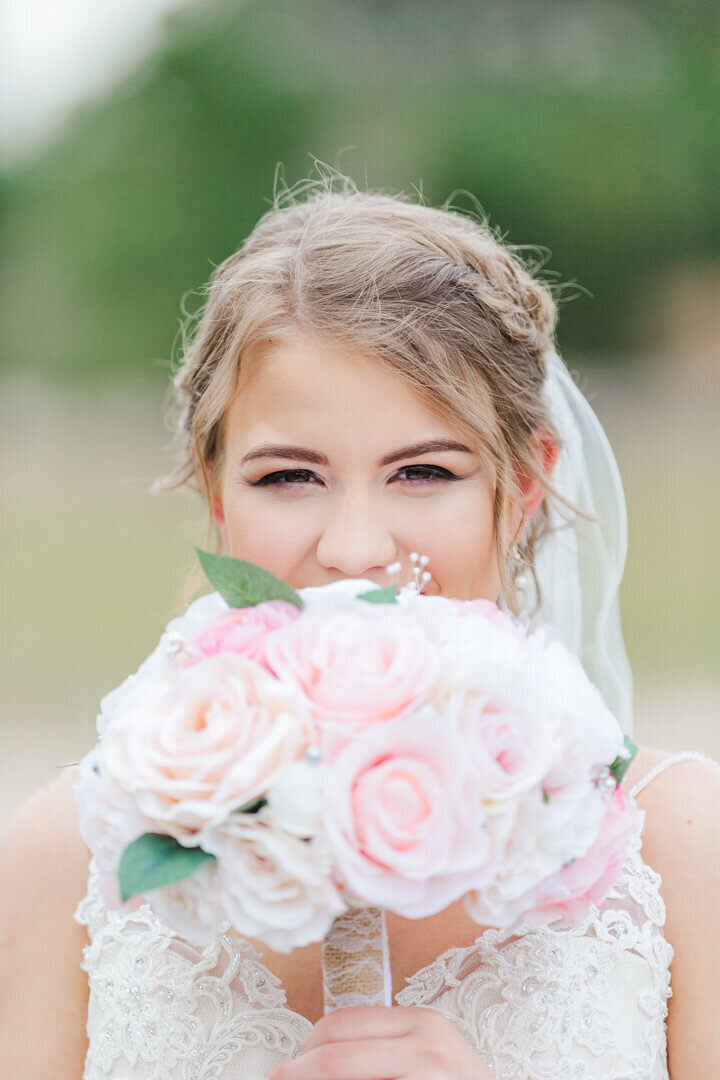 A close up photo of a bride with her pink bouquet staring into the camera. Captured by wedding photographer Photography by Karla.