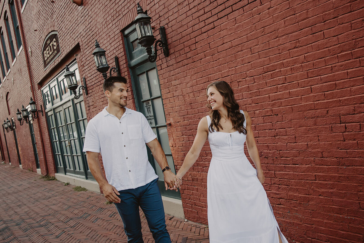 A couple holding hands and walking down a brick sidewalk 