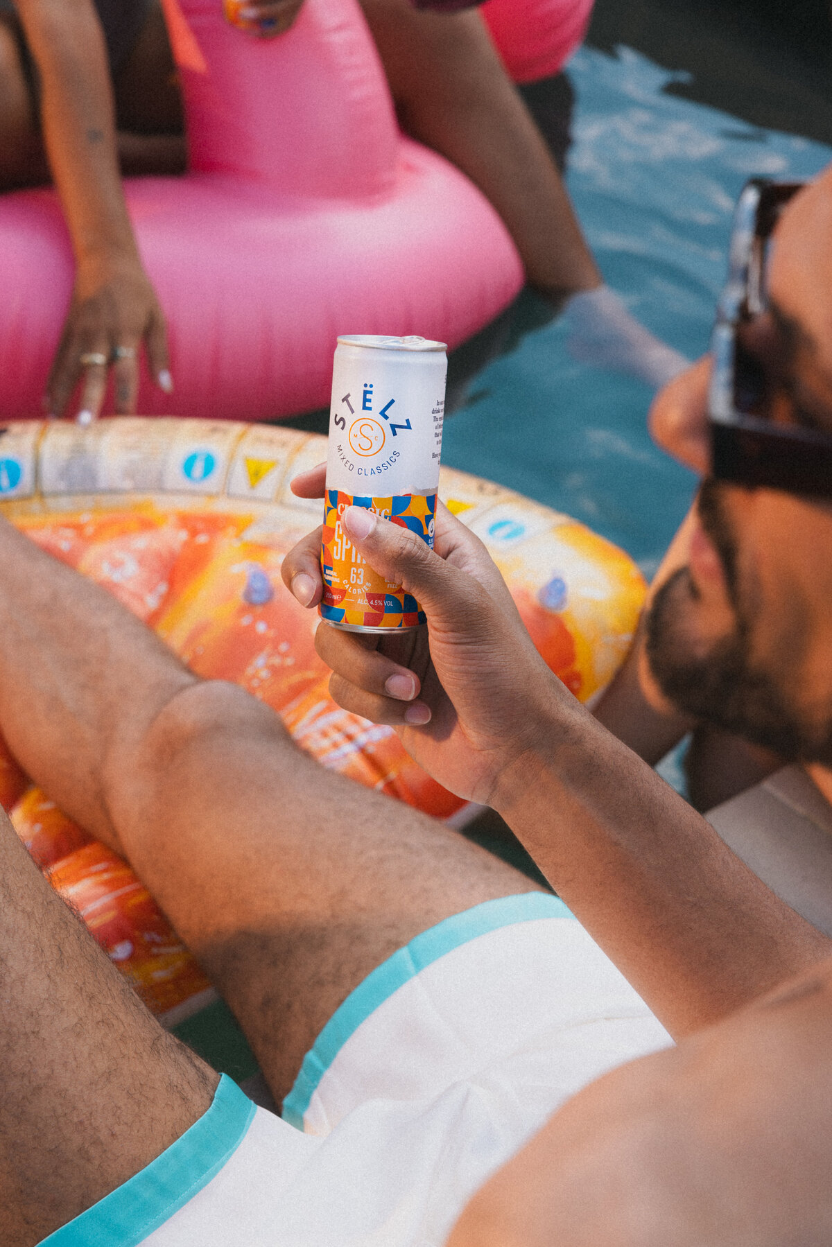 A person holding a can of Stëlz Classic Spritz while lounging on a pool float. The relaxed vibe is enhanced by the vibrant colors of the float and the refreshing beverage. Photographed by Bo Eppink