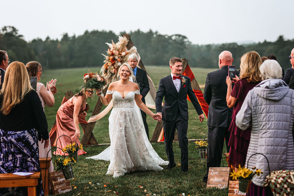 Bride and Groom exit down the aisle after ceremony laughing and smiling in beautiful field at Sanborn Hill Farm NH By Lisa Smith Photography