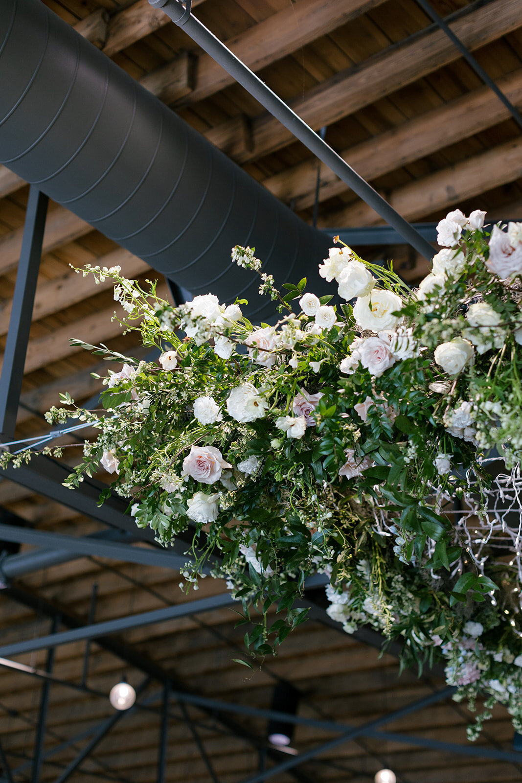 Lush floral chandelier lights up the dance floor with florals of petal heavy roses, ranunculus, lisianthus, delphinium, and dark greenery in hues of white, cream, and blush. Designed by Rosemary and Finch in Nashville, TN.
