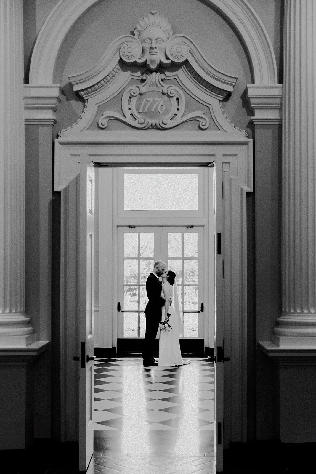 A large ornate door, peaking through door we see the couple kissing.