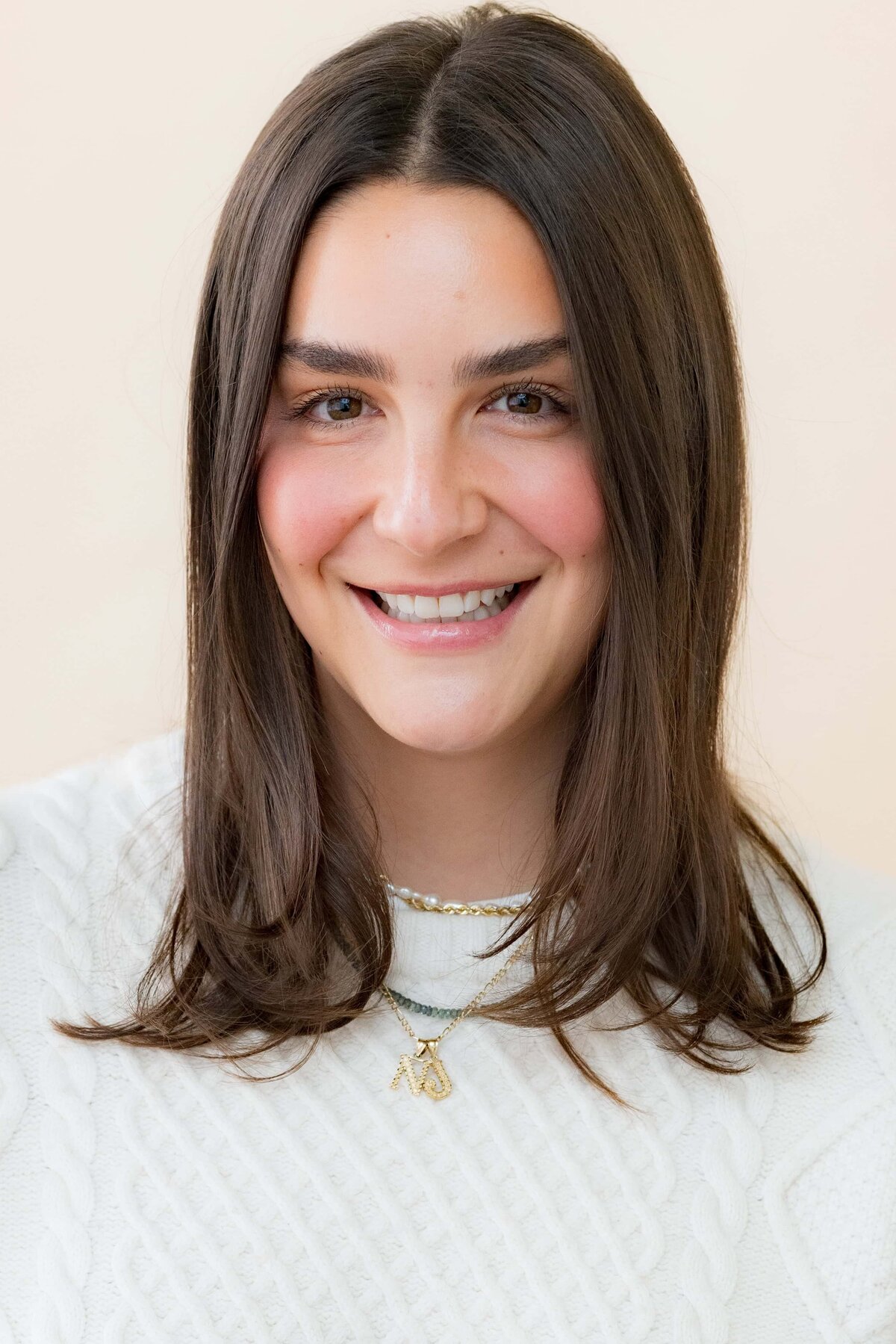 Young woman with long dark hair smiling for a photo in a light colored sweater