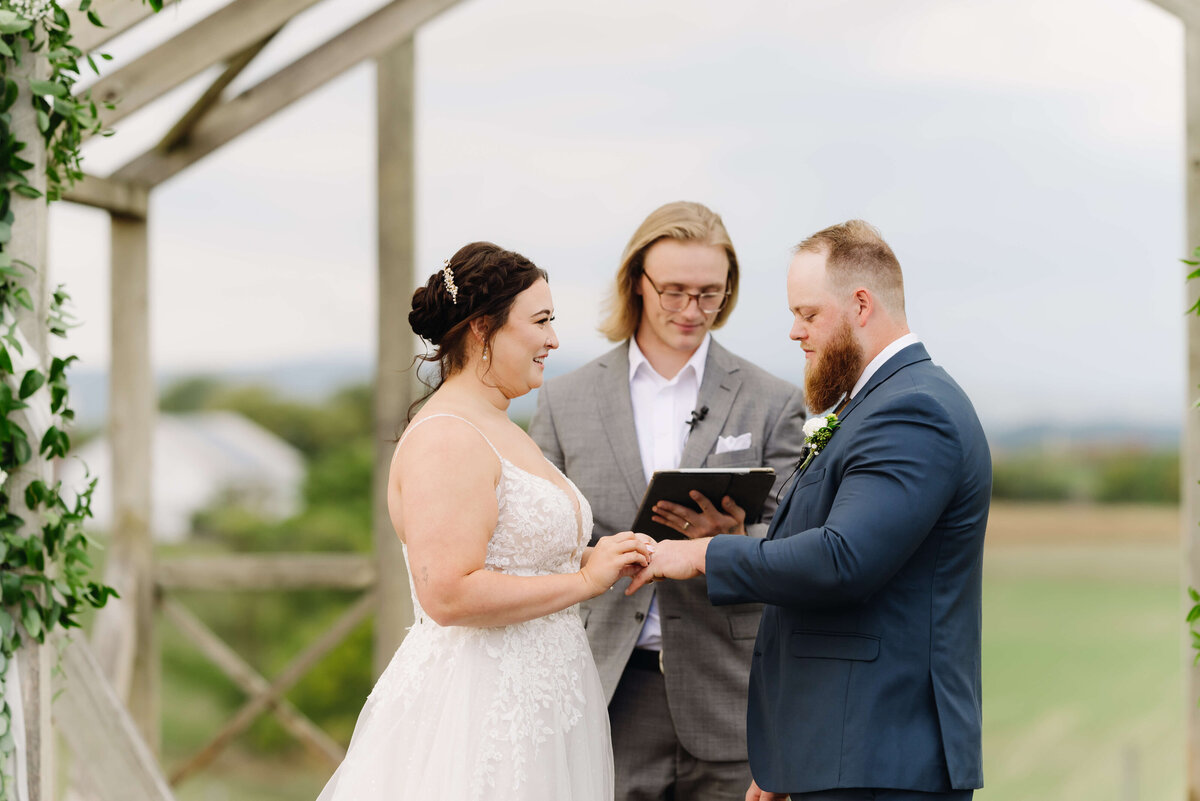 bride and groom holding hands during their outdoor wedding ceremony at Sunny Slope Farm while their officiant reads to them captured by Charlottesville wedding photographer