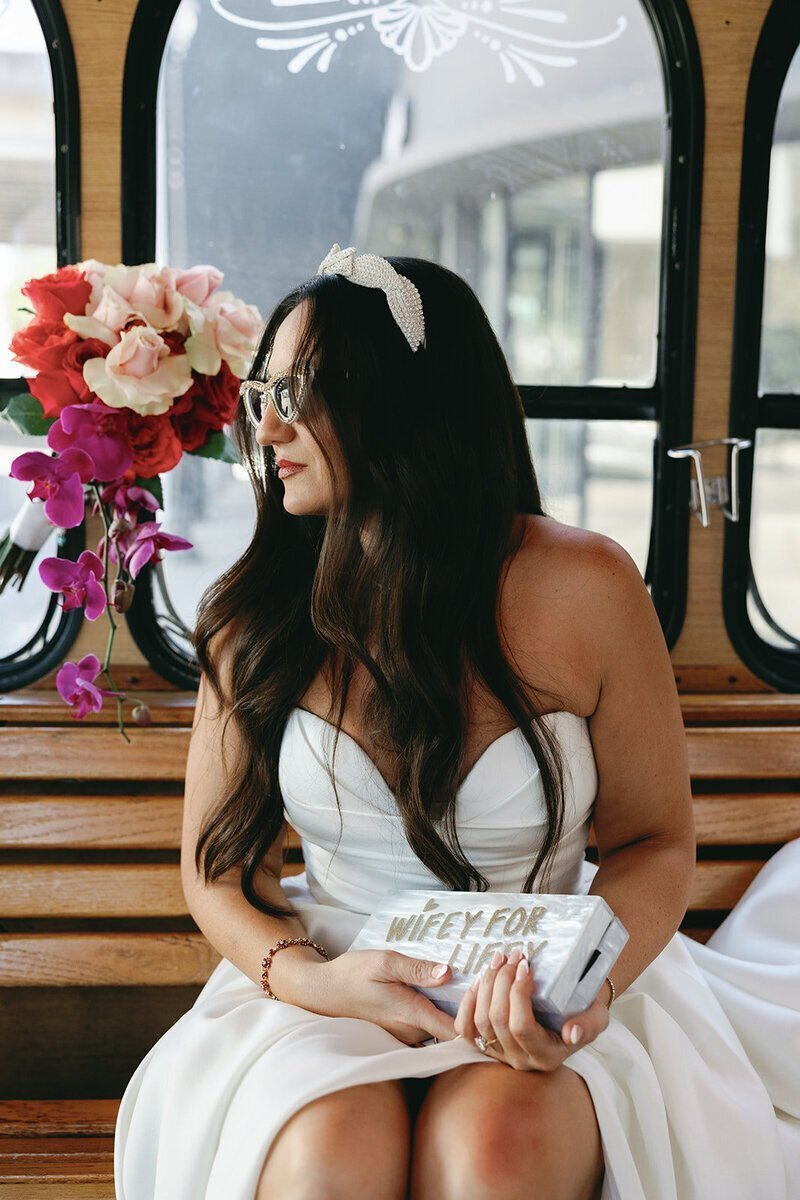 bride sitting on boat in front of flowers holding bag at the penthouse at riverside wharf​