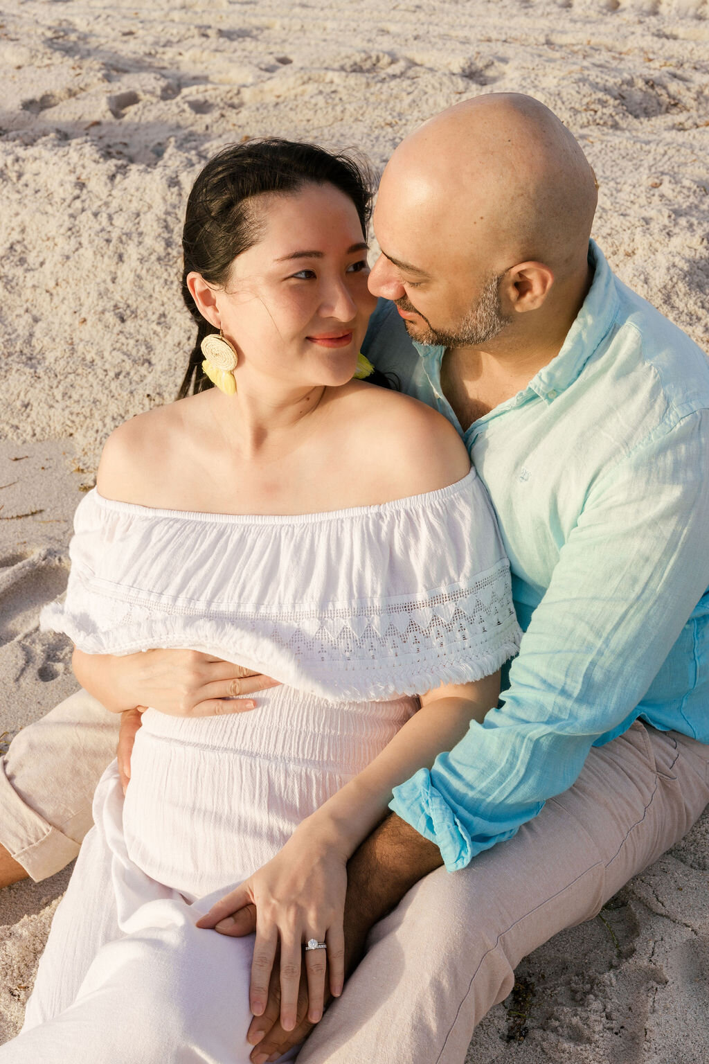 Couple sitting close on the sand during their maternity session in Miami Beach, South Florida.