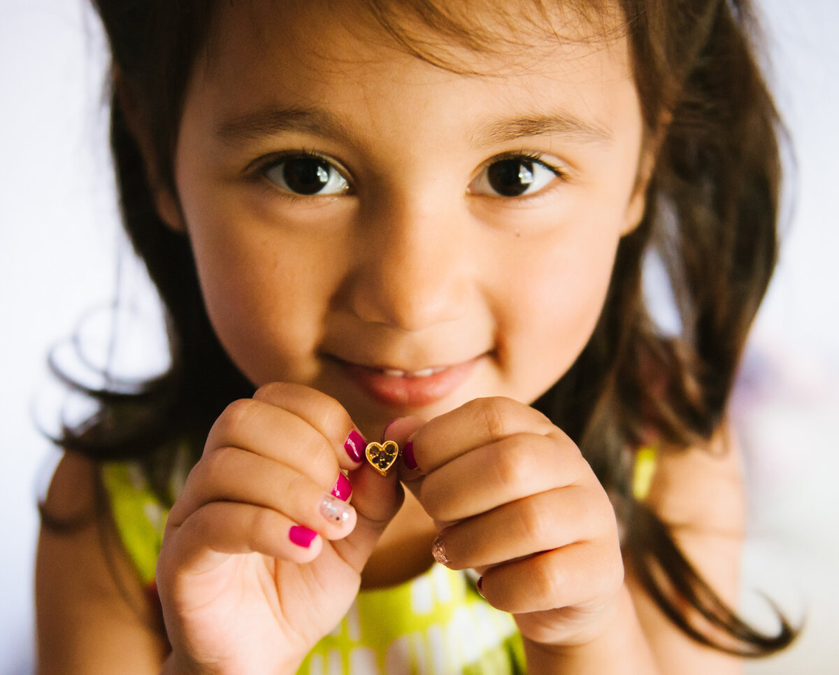 A child smiling while holding out a heart shaped necklace.