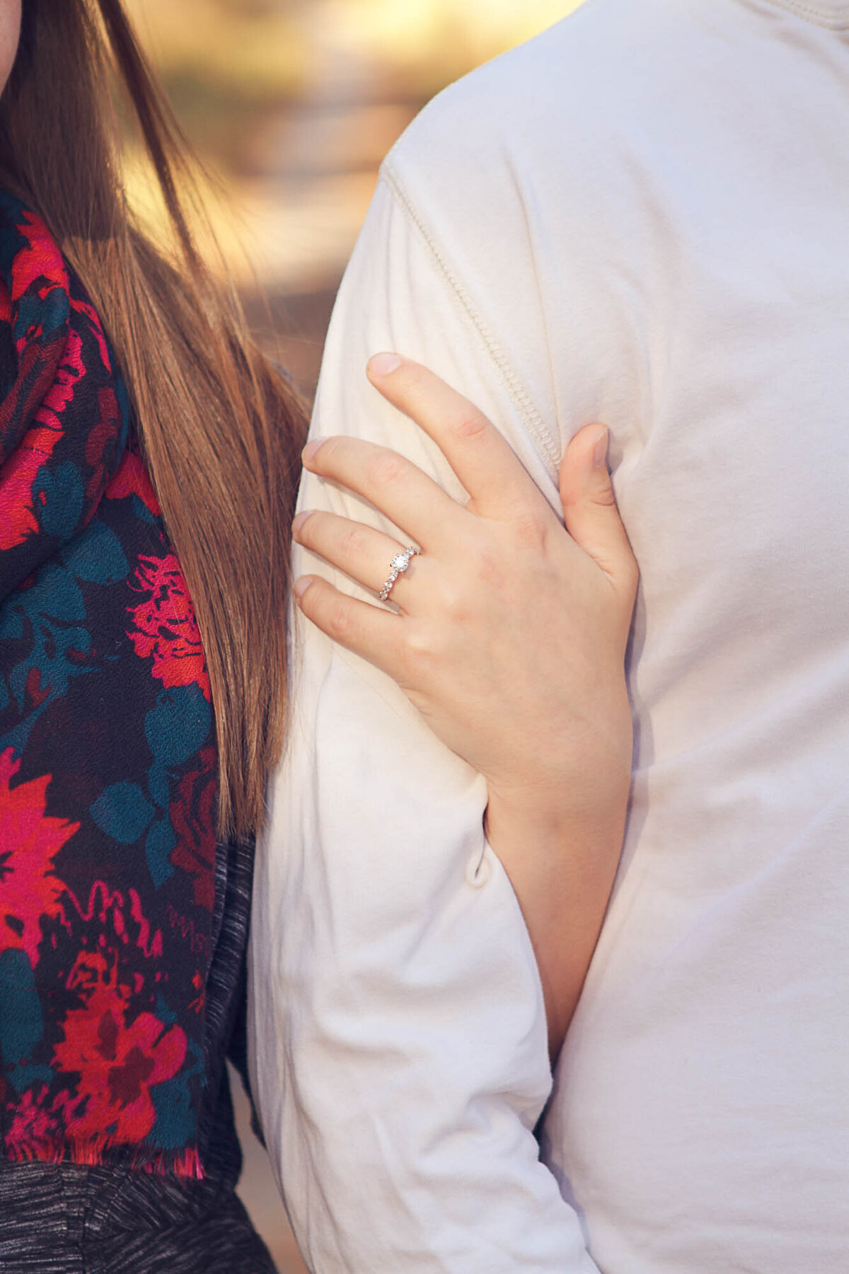 Closeup portrait of her engagement ring as she holds his arm.