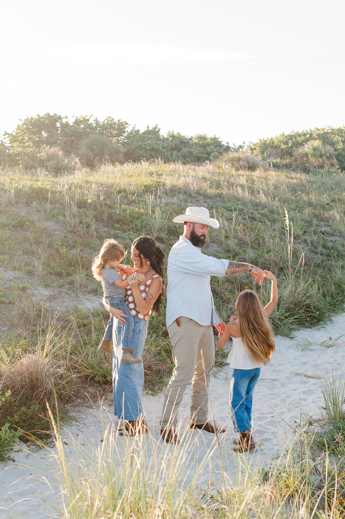 Family standing on a beach path near the dunes dancing at sunset