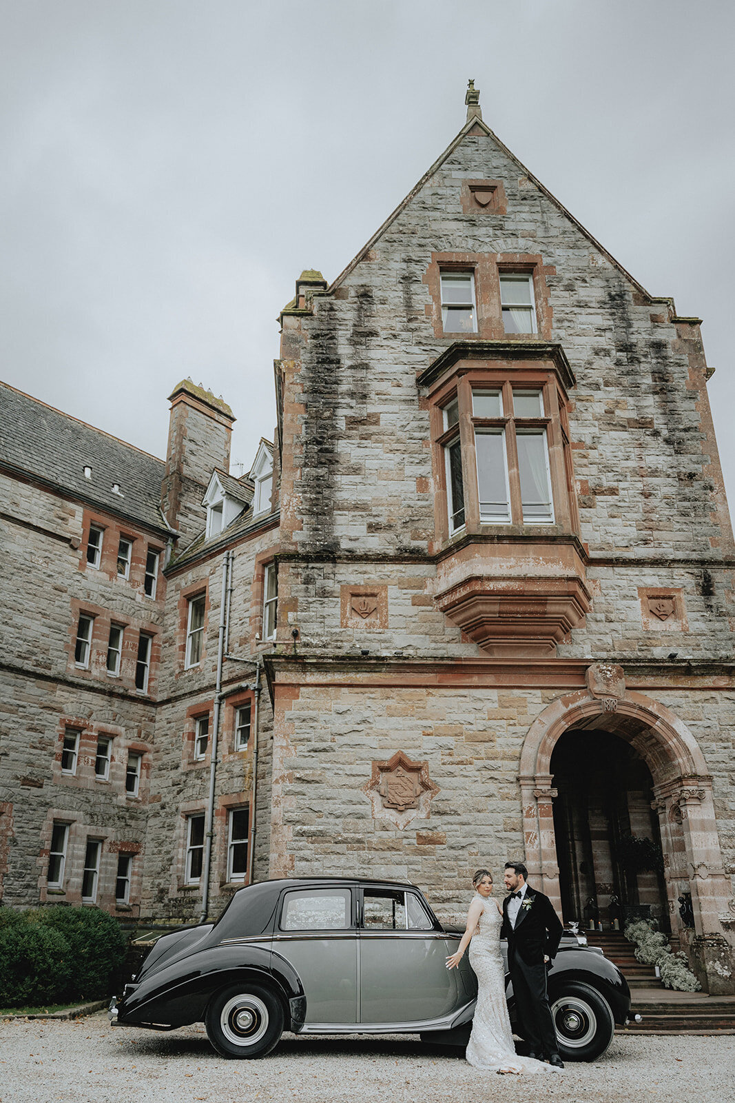 Bride and groom leaning against old car in front of Ireland castle