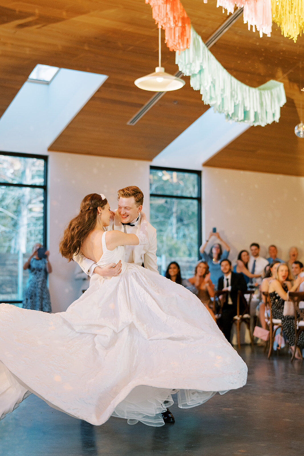 The groom swings his bride around in his arms for their first dance in the modern reception space at The Grand lady