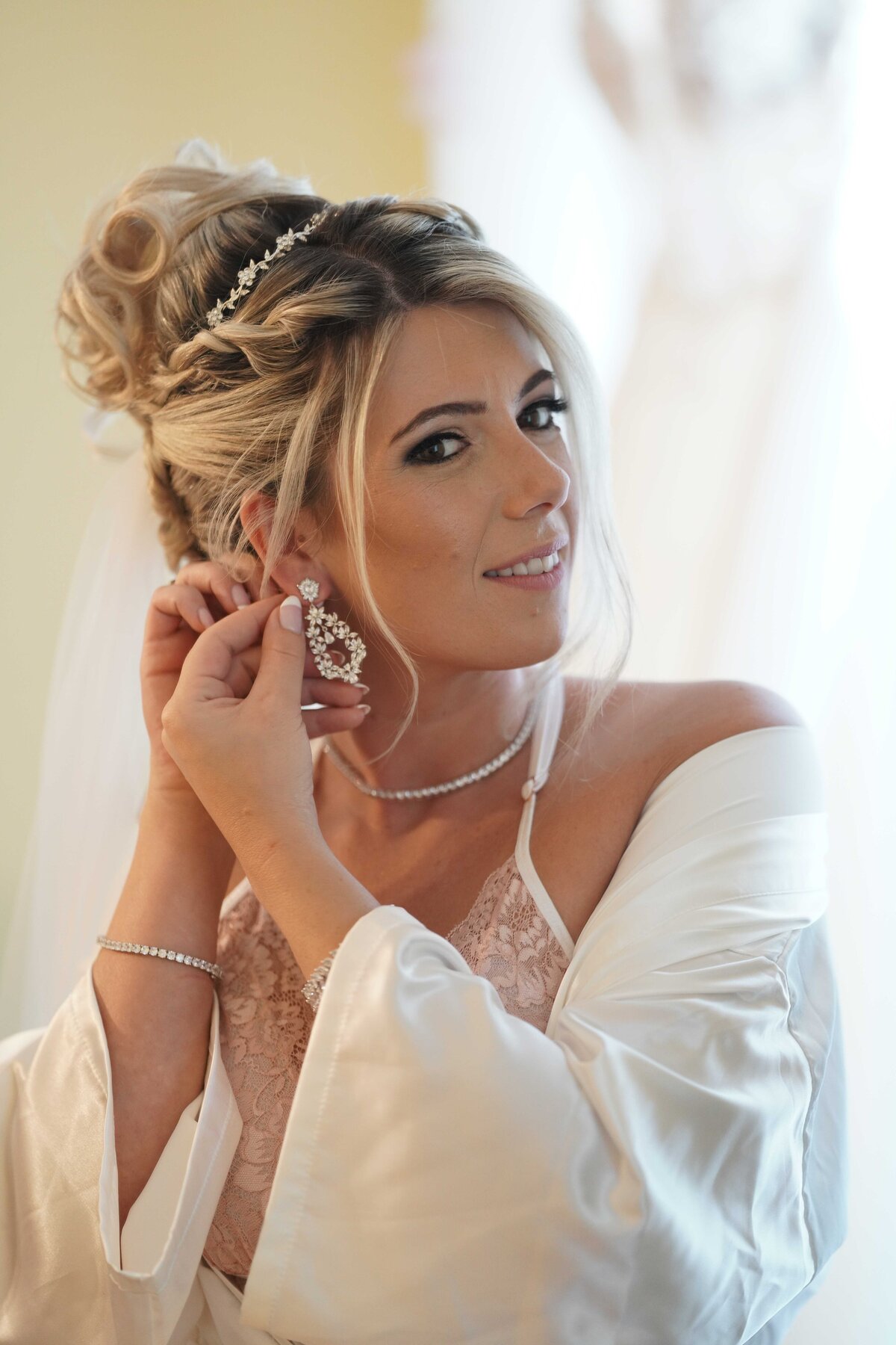 A bride delicately puts on her earrings, adding the final touch to her elegant bridal look. This close-up image highlights the intricate details of her accessories and her graceful preparation, capturing the refined elegance and personal moments of her wedding day.